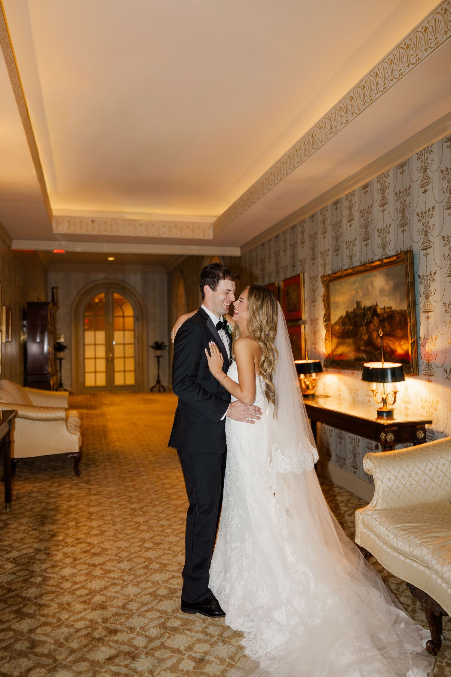 Newlyweds share an intimate moment in an elegantly decorated hotel room with warm lighting.