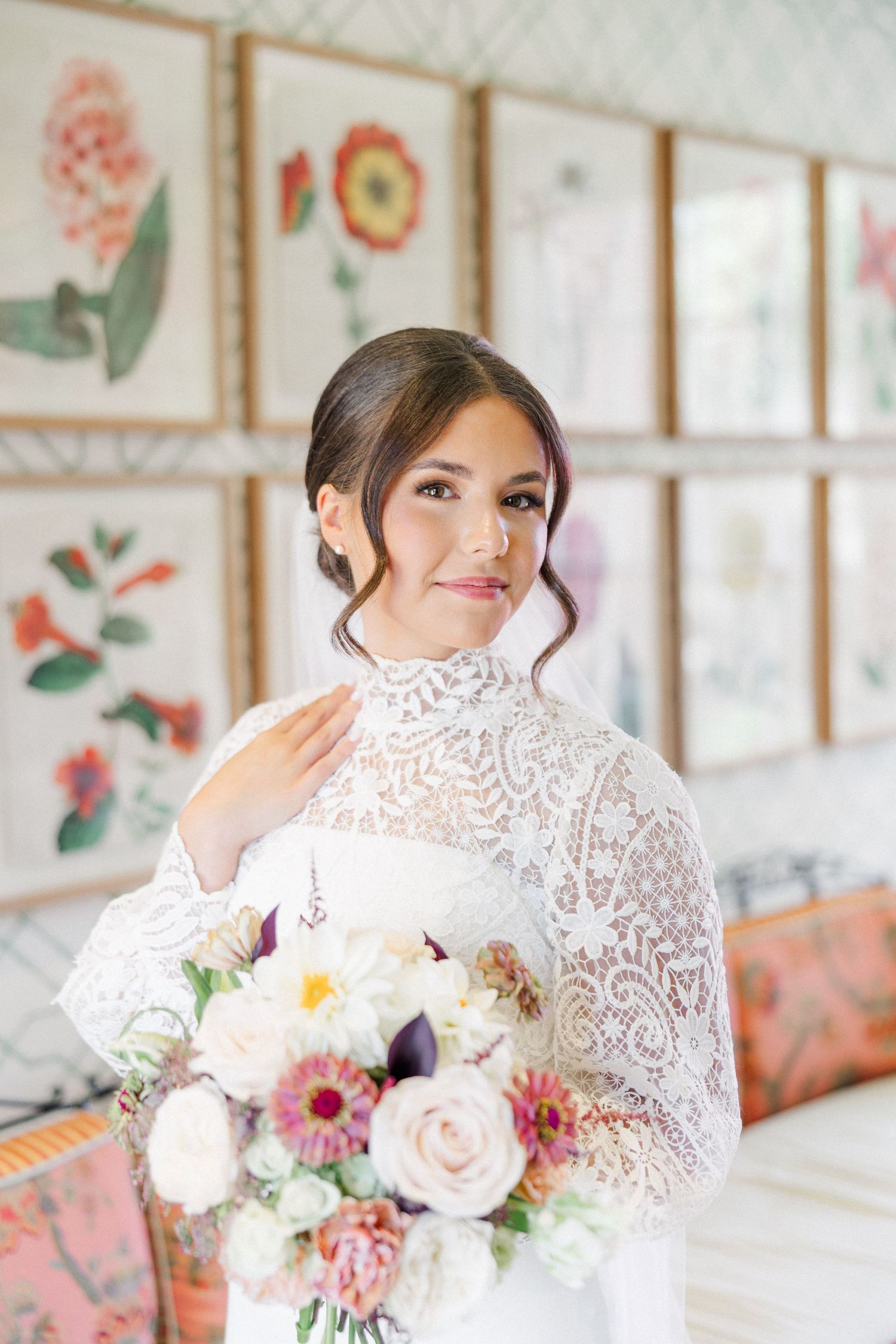 A bride in a delicate white lace gown holds a romantic bouquet of pink and white flowers against a light-filled backdrop.