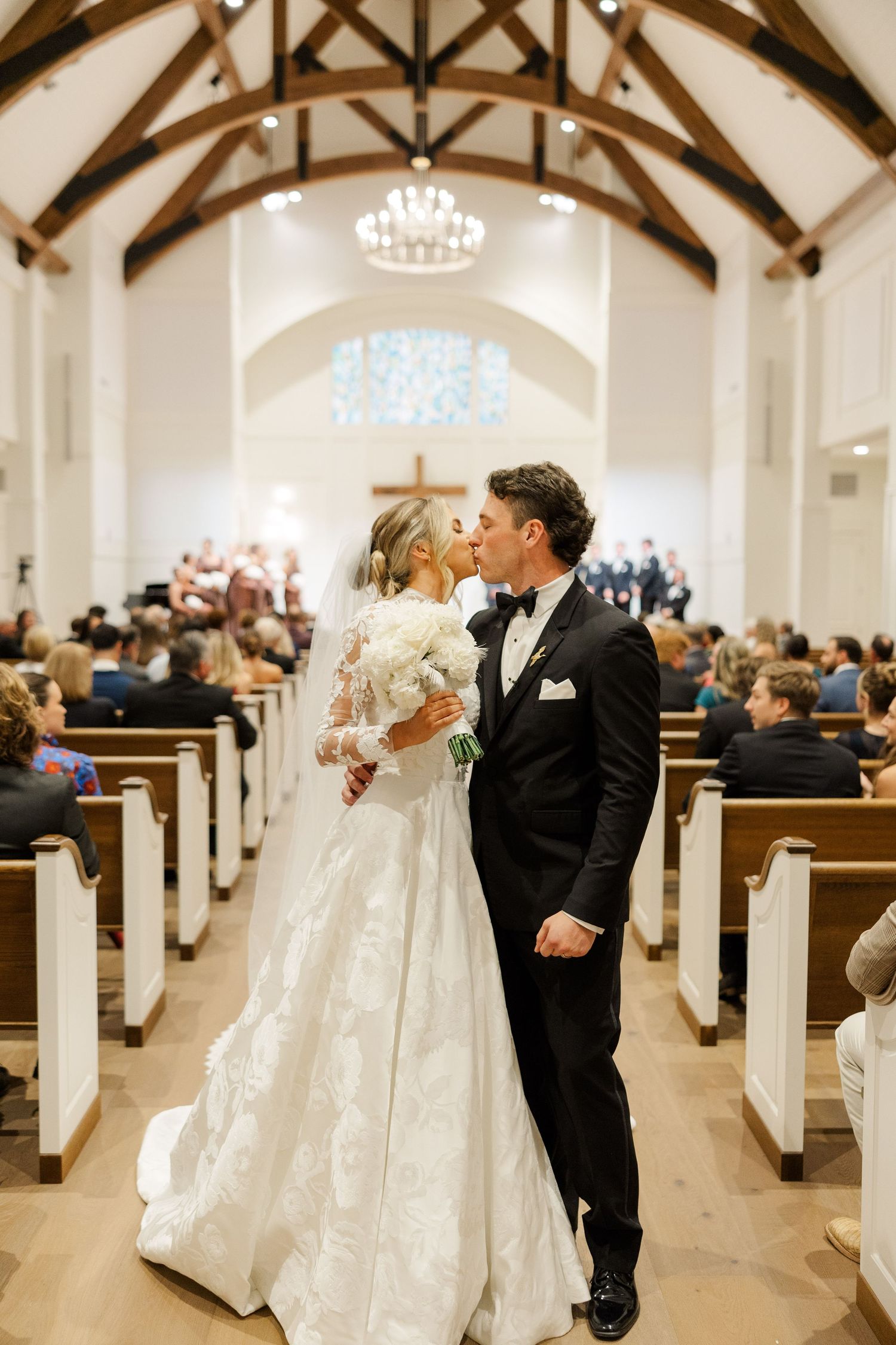 Wedding ceremony in traditional church with wooden beam ceiling and white pews.