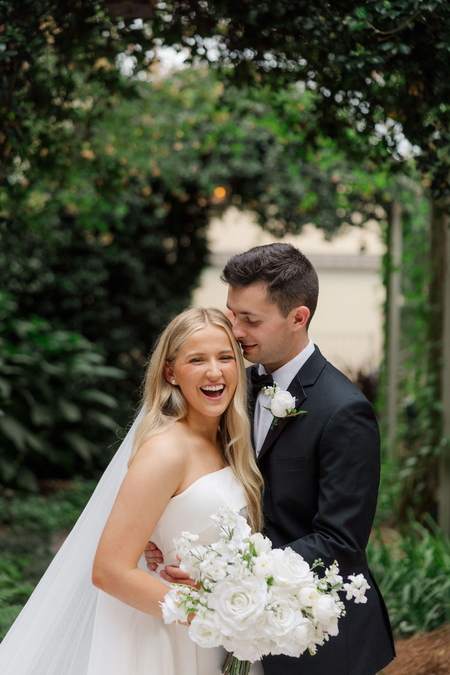 Joyful wedding couple sharing a candid moment outdoors surrounded by lush greenery.