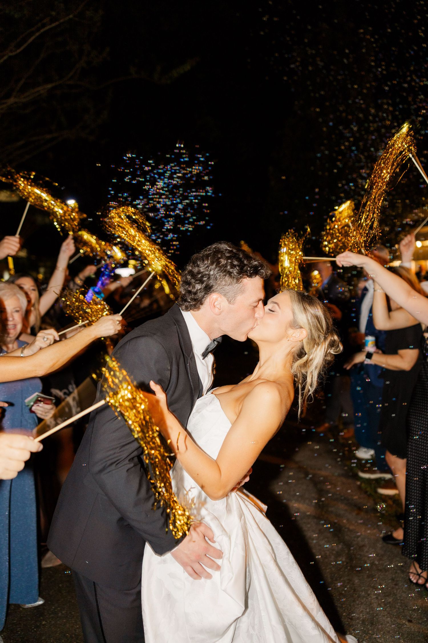 Newlyweds share a romantic kiss during sparkler exit at nighttime celebration.