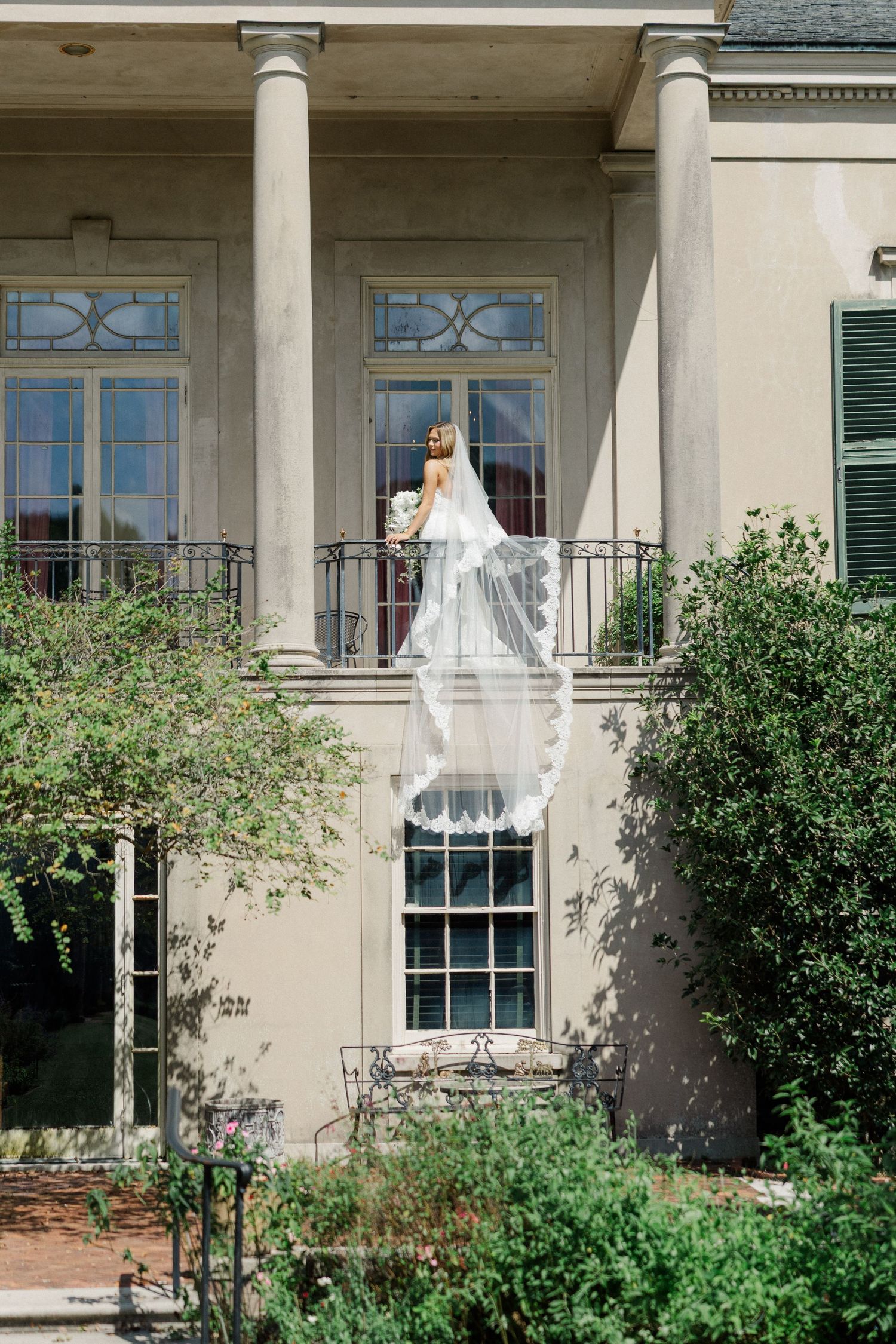 Classic southern mansion wedding photo with columns and balcony creating elegant architectural frame.