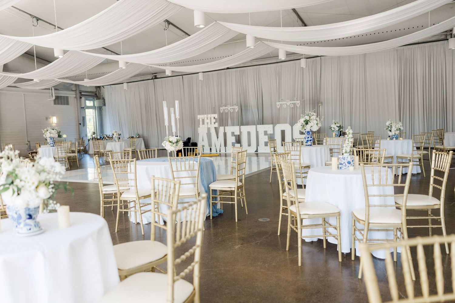 A panoramic view of an elegant white wedding reception venue with round tables and chiavari chairs set for a celebration.