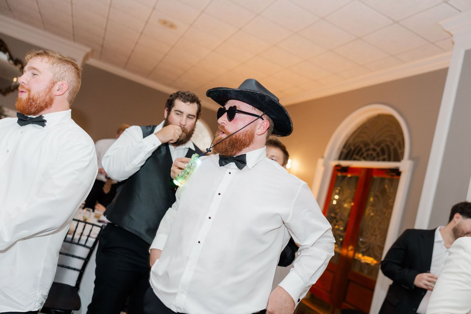 Wedding reception guests dance and celebrate under indoor lighting.