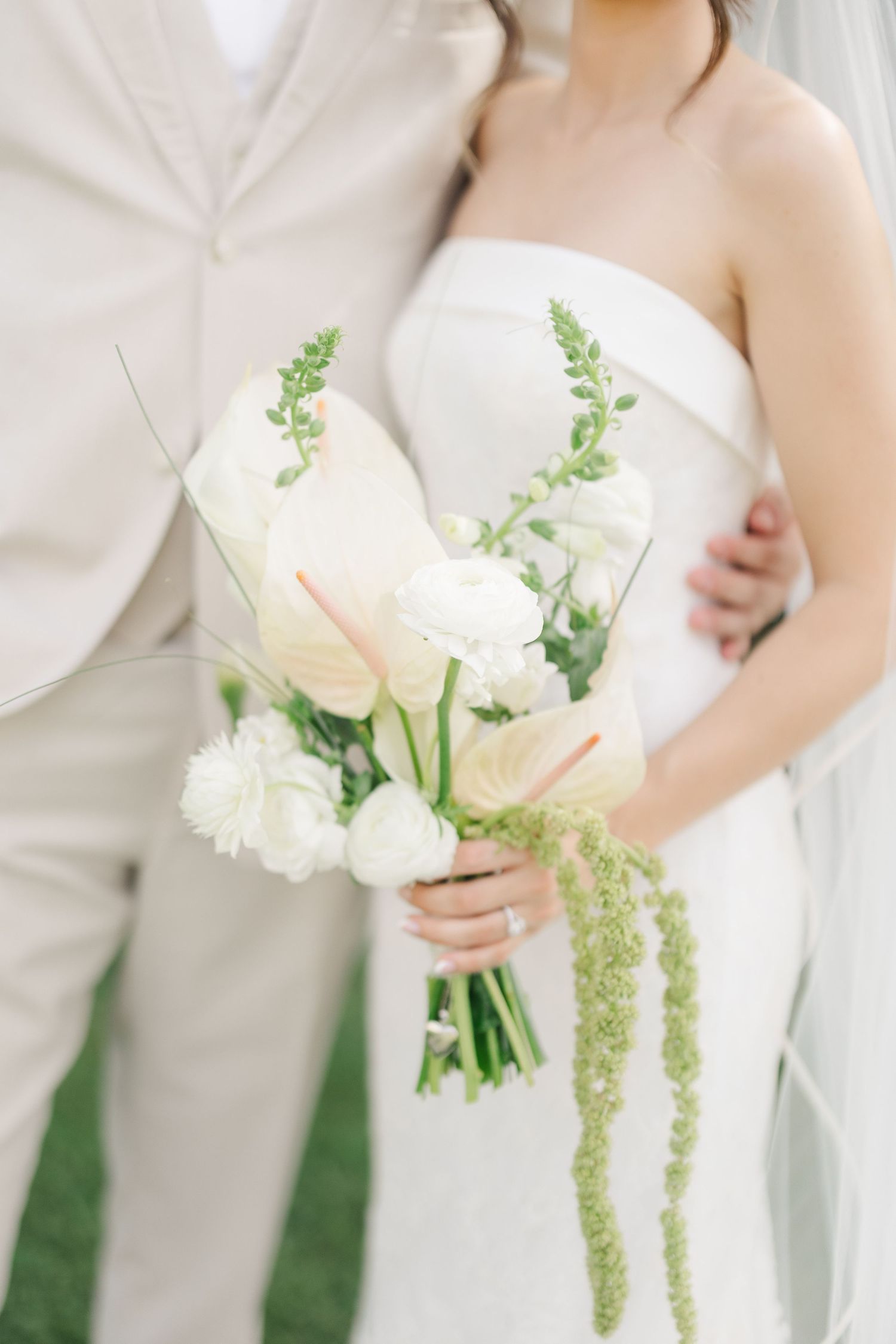 Close-up of bride holding elegant white bouquet with anthurium and trailing green amaranthus.