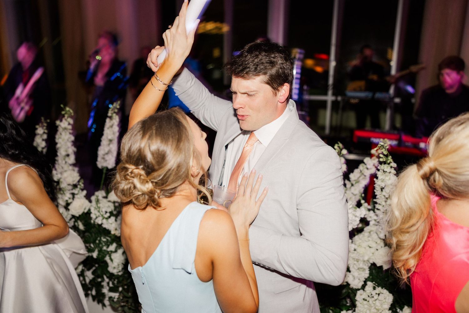 Couple dancing at wedding reception surrounded by white floral arrangements and live band performance.
