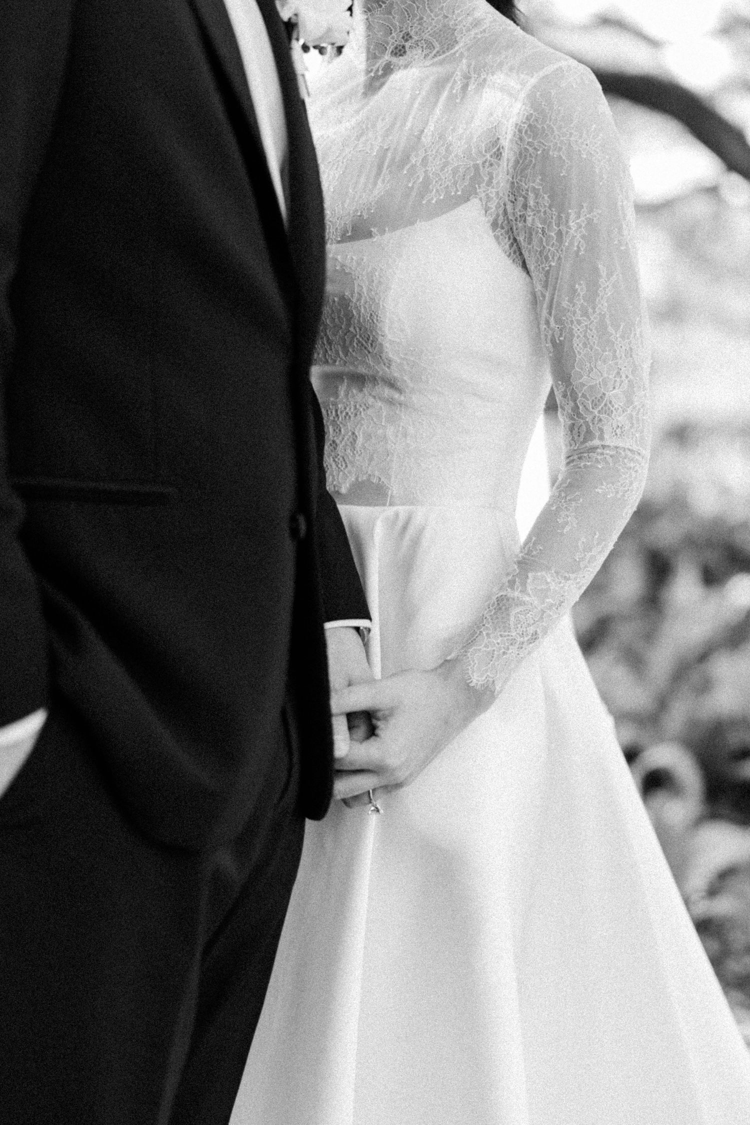 Black and white close-up of bride in lace wedding dress standing beside groom in black tuxedo.