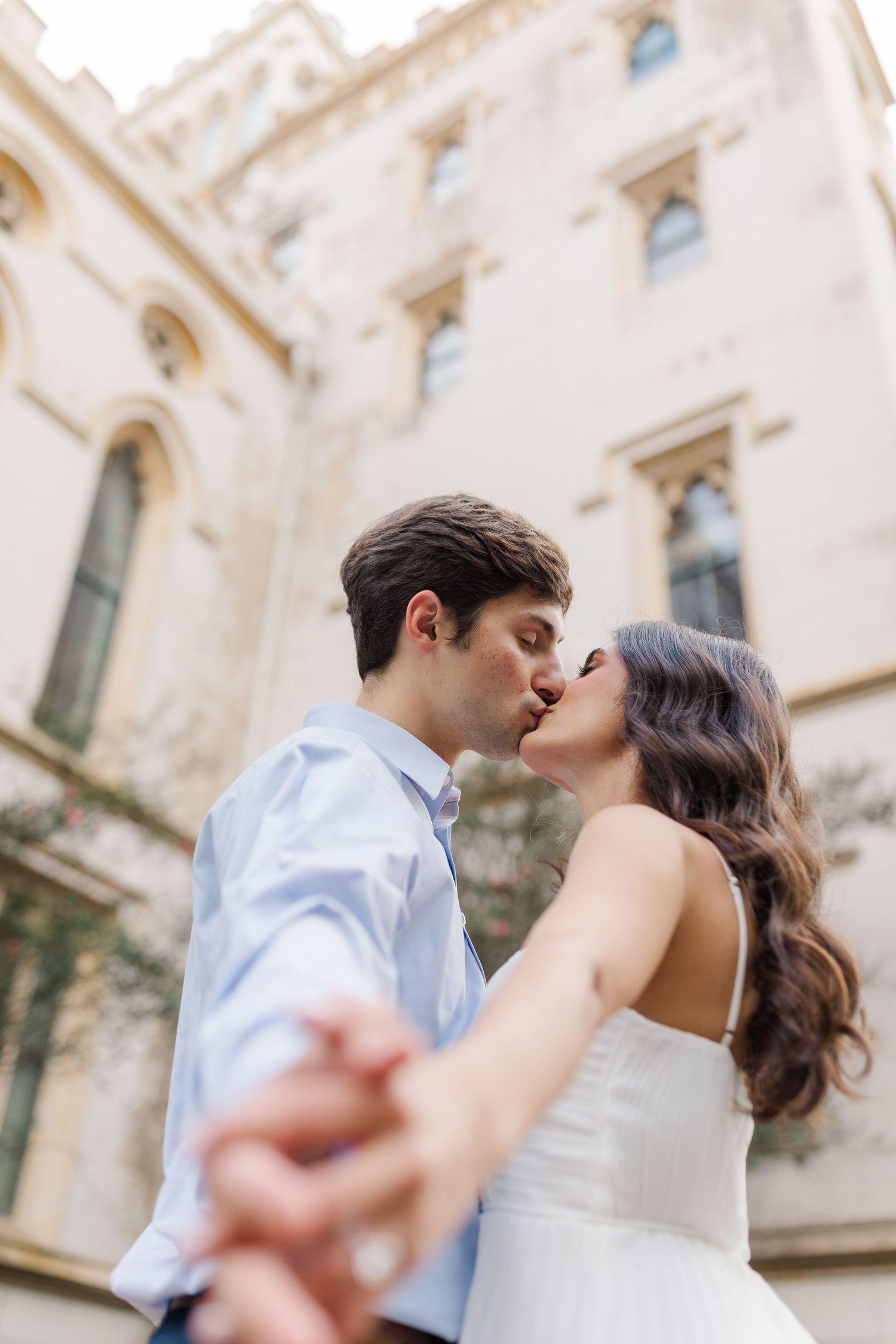 Couple shares a romantic kiss in front of a historic stone building with elegant architecture.