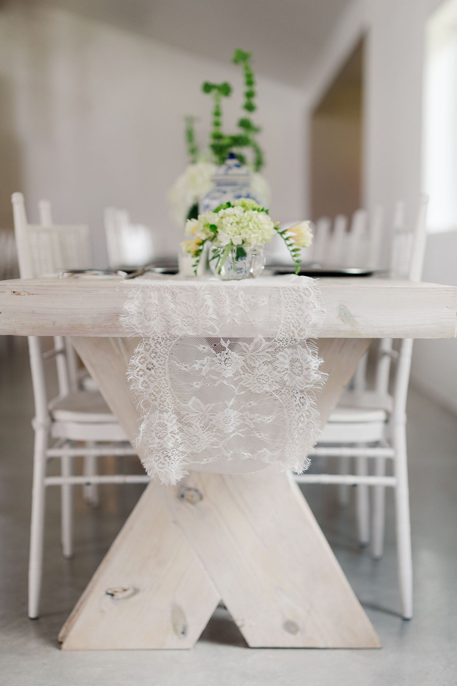 Rustic wooden farmhouse table with lace runner and white floral centerpieces for an elegant wedding reception.