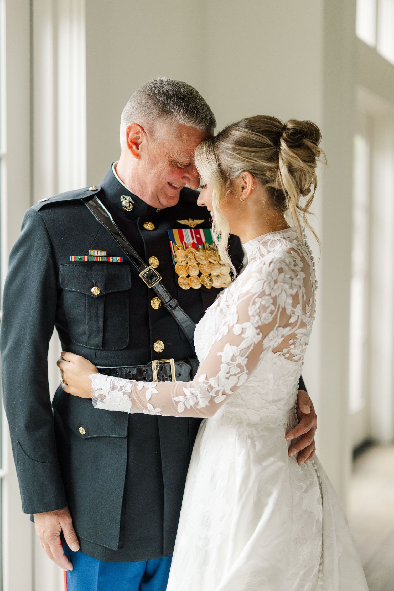 A touching first look moment between a Marine in dress uniform and bride in a lace gown against a bright window.