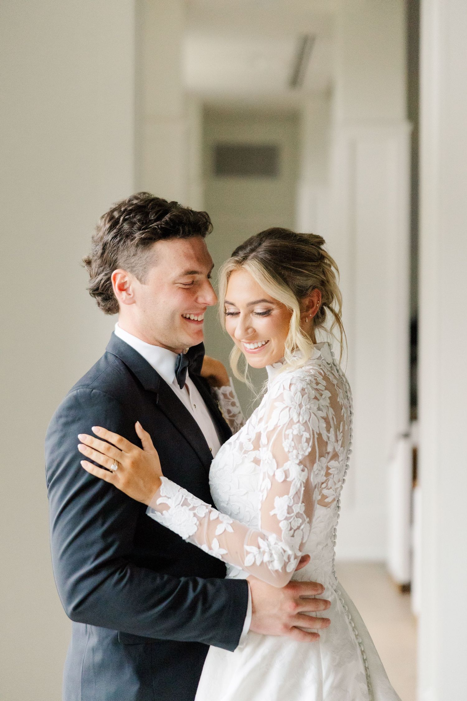 A romantic first look moment between newlyweds as they embrace in a bright indoor setting with white columns.