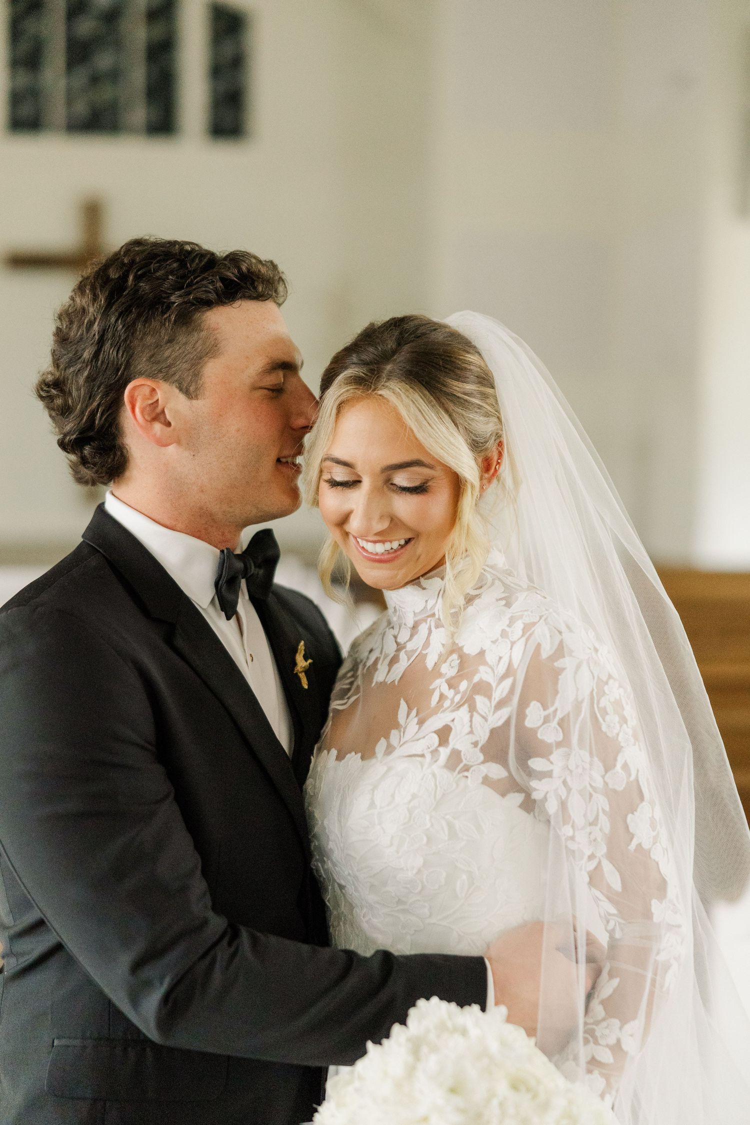 Romantic wedding couple shares intimate moment with bride in lace veil and groom in black suit.