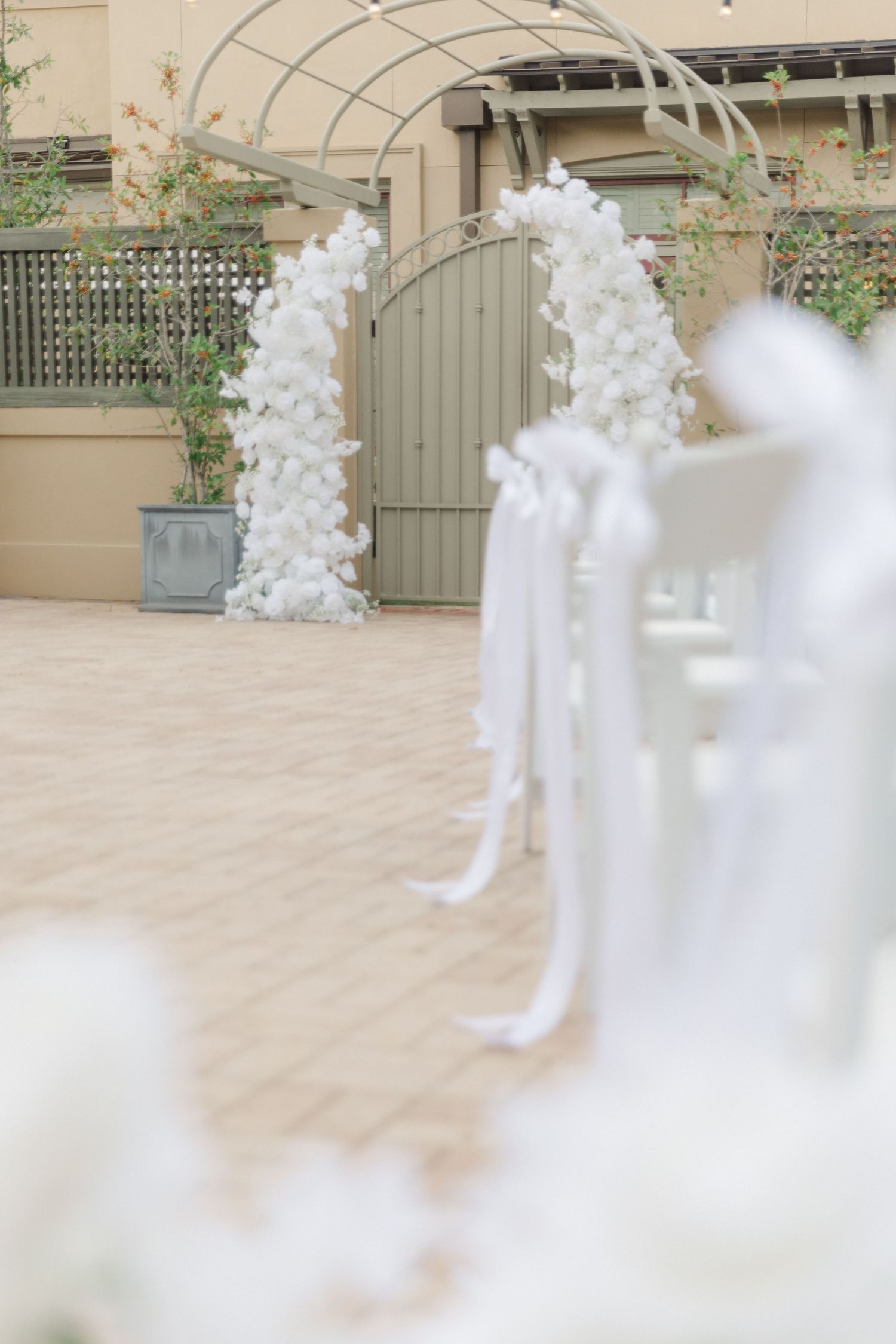 White floral wedding arch decorations against a beige wall at an outdoor venue.