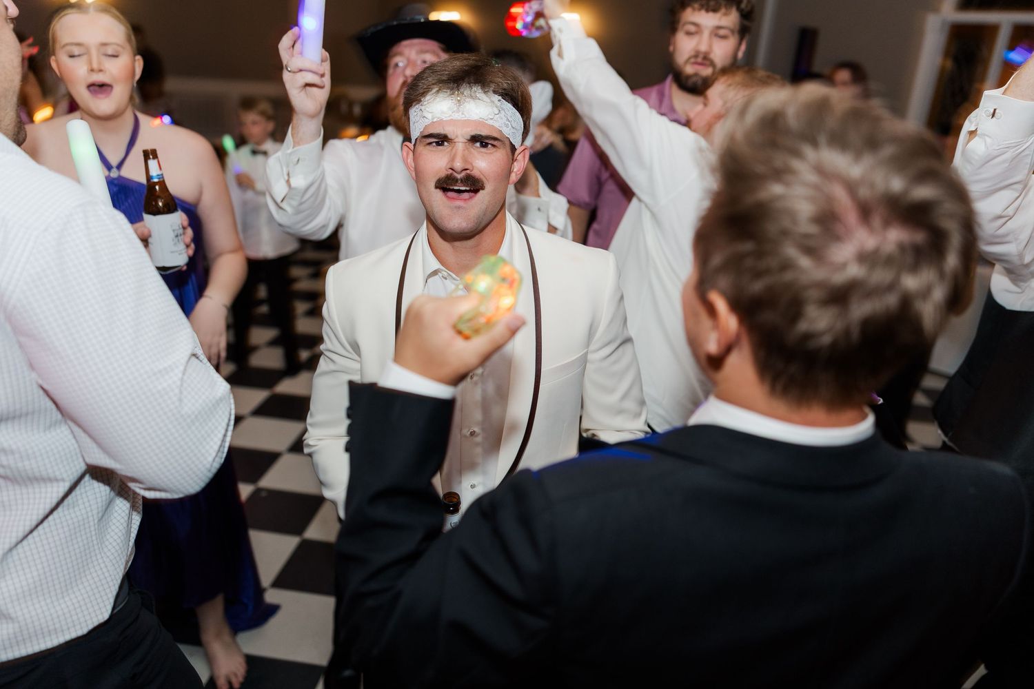 Energetic wedding reception dancing on black and white checkered floor.