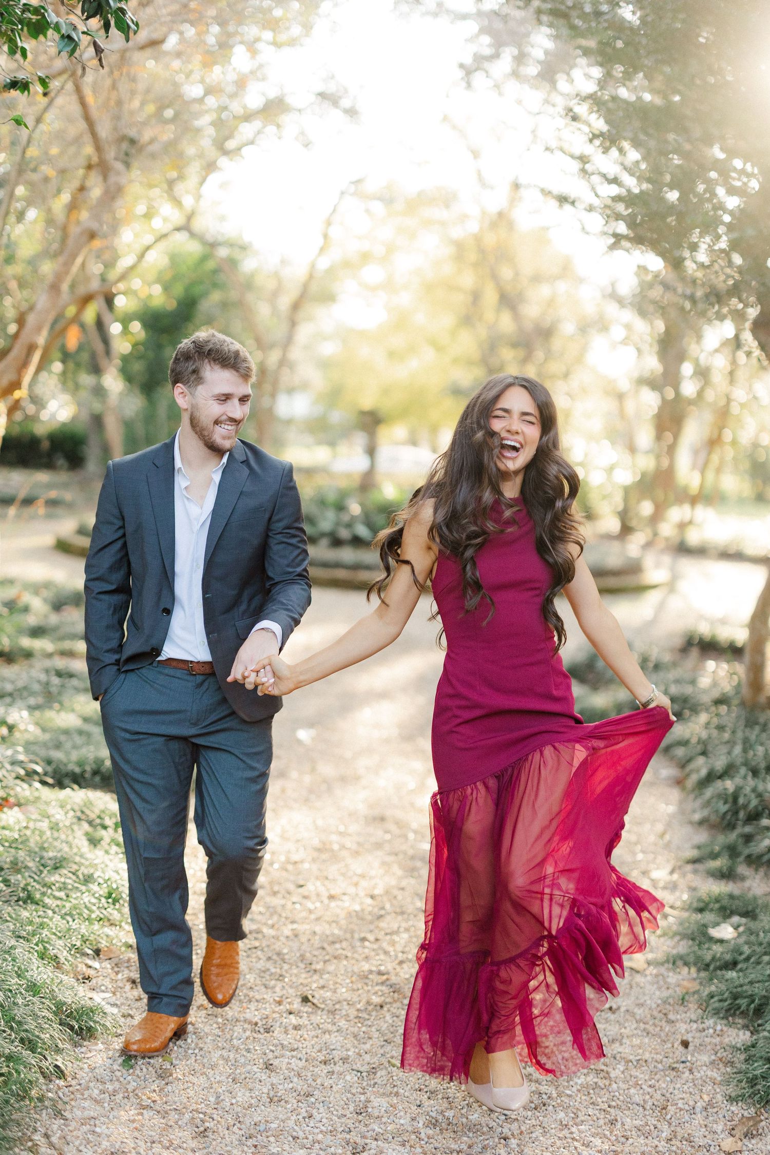 A playful couple dances and twirls on a garden path during a sunny afternoon photoshoot.
