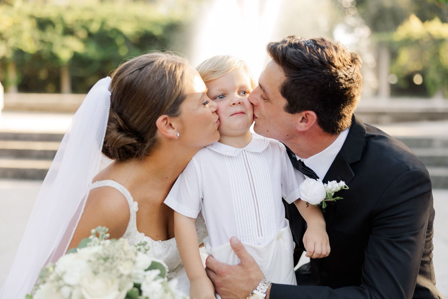 A couple shares intimate wedding day moments with their young child outdoors.