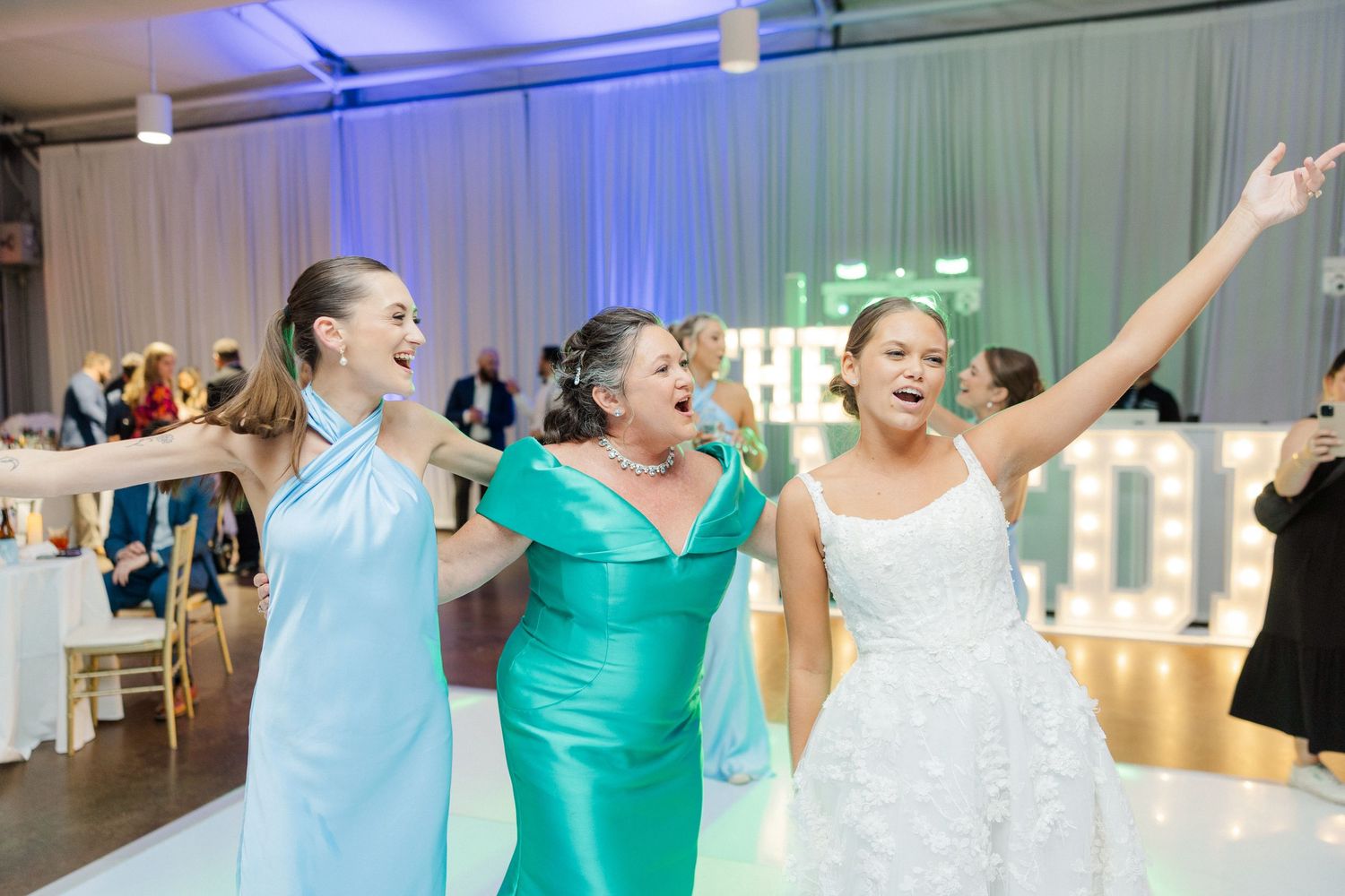 Wedding reception with blue lighting and bridesmaids in turquoise dresses celebrating.