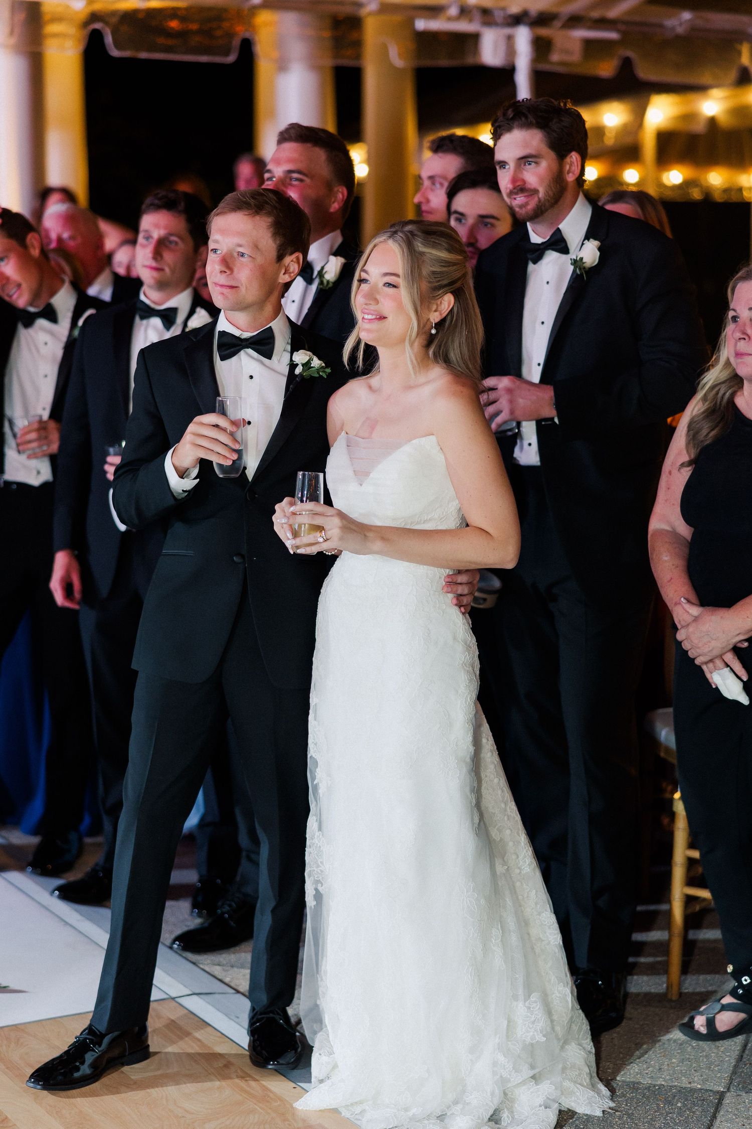 Wedding guests in formal attire gather during an evening reception celebration.