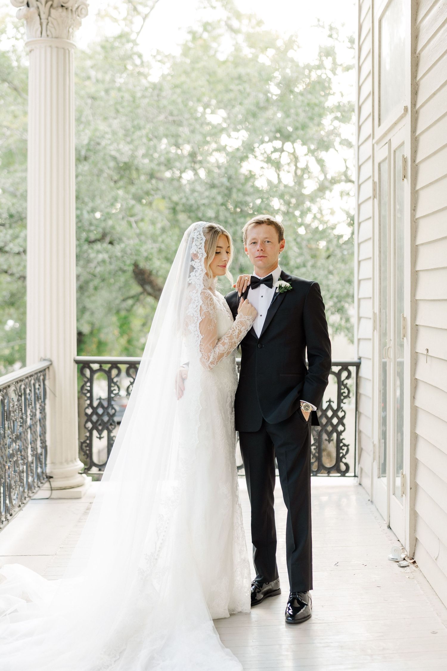 Wedding couple poses together on a classic Southern mansion's white columned veranda in natural light.