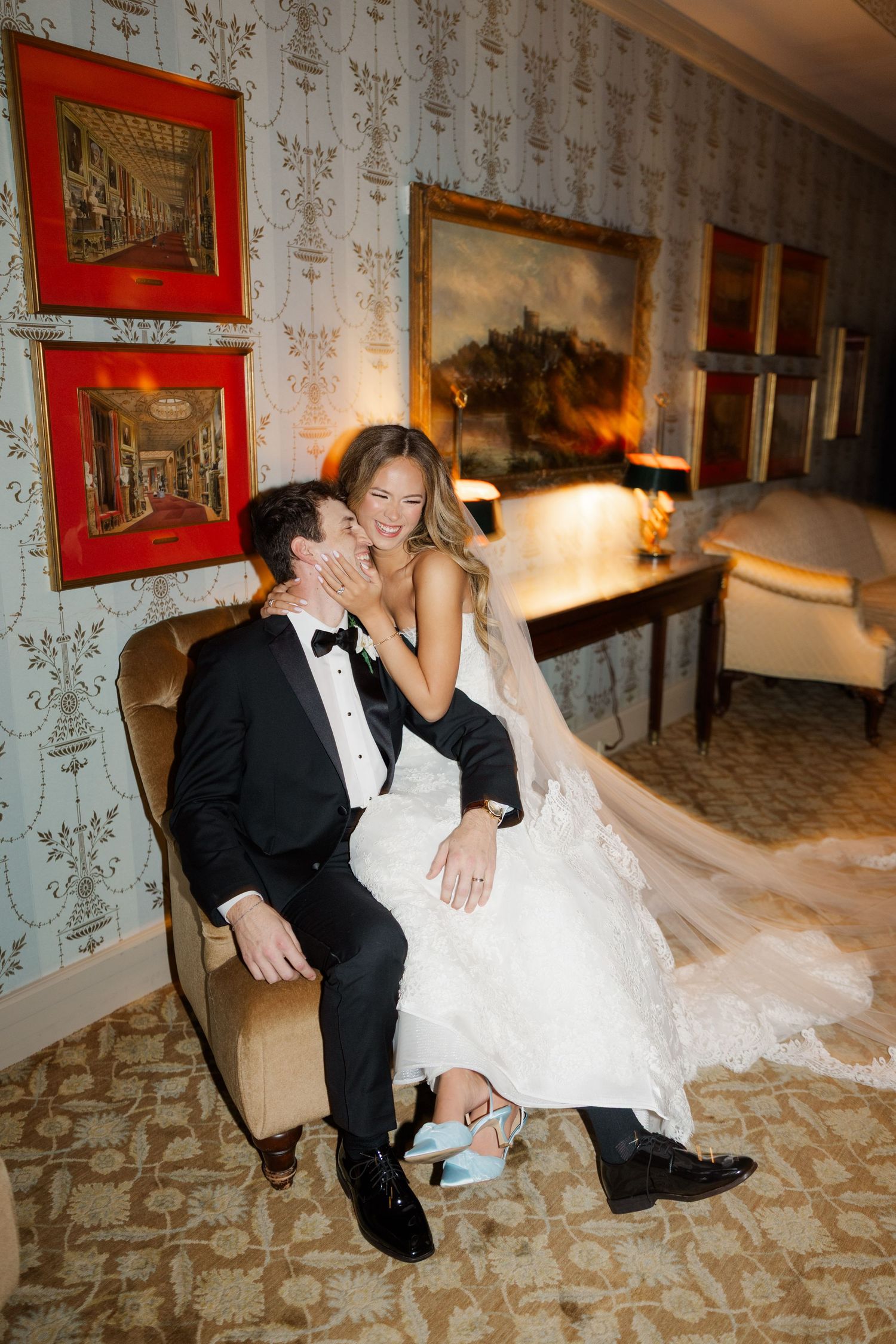 Romantic wedding photos taken in an elegant room with vintage wallpaper and red framed artwork.