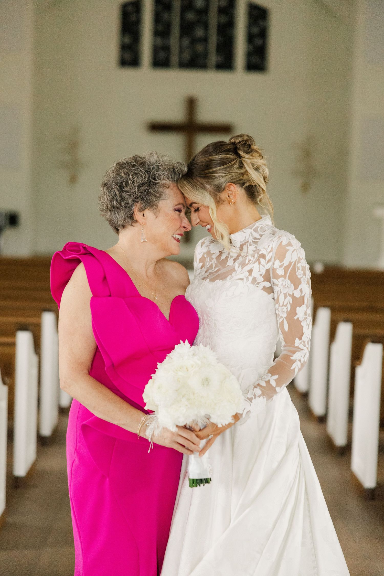 Emotional wedding moment captured in a bright church interior with pink and white attire.