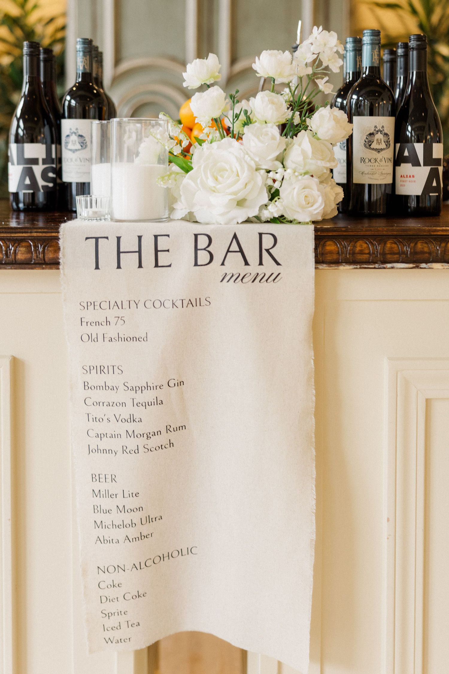 Bar menu display with white floral decorations and drink list showing specialty cocktails and spirits.