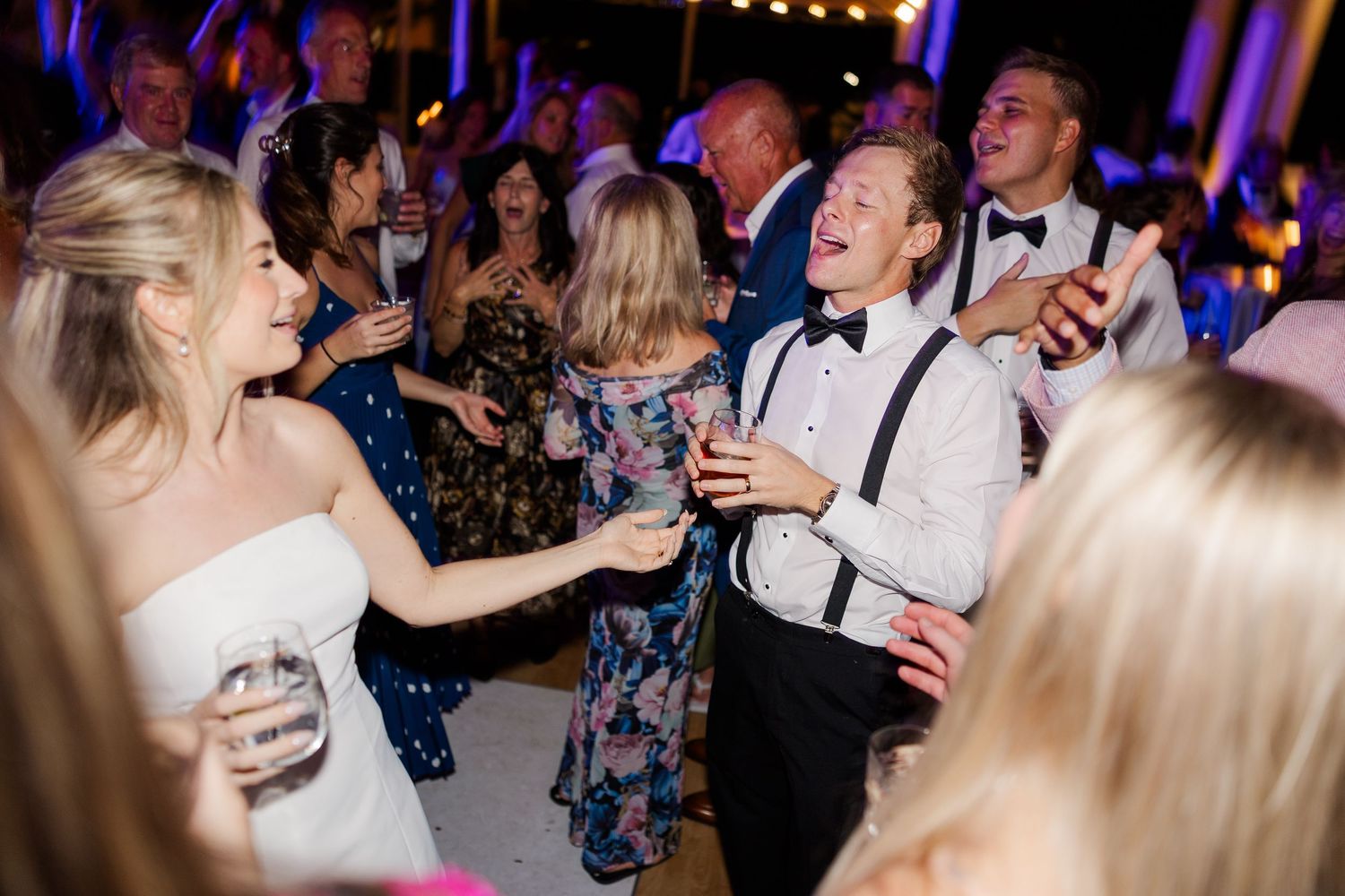 Wedding reception dance floor filled with guests celebrating under purple lighting.