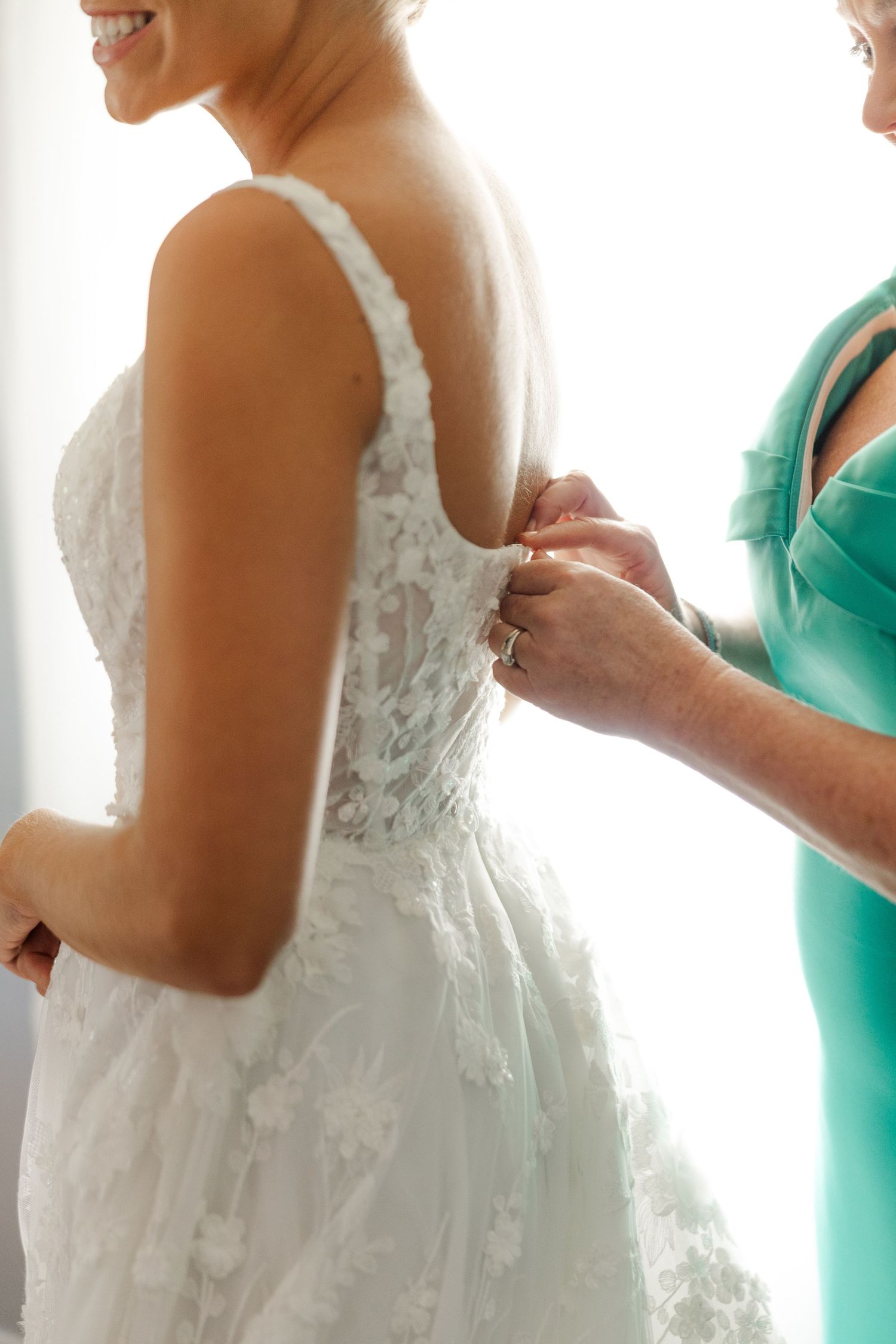Close-up view of a white lace wedding dress being buttoned up in soft natural light.