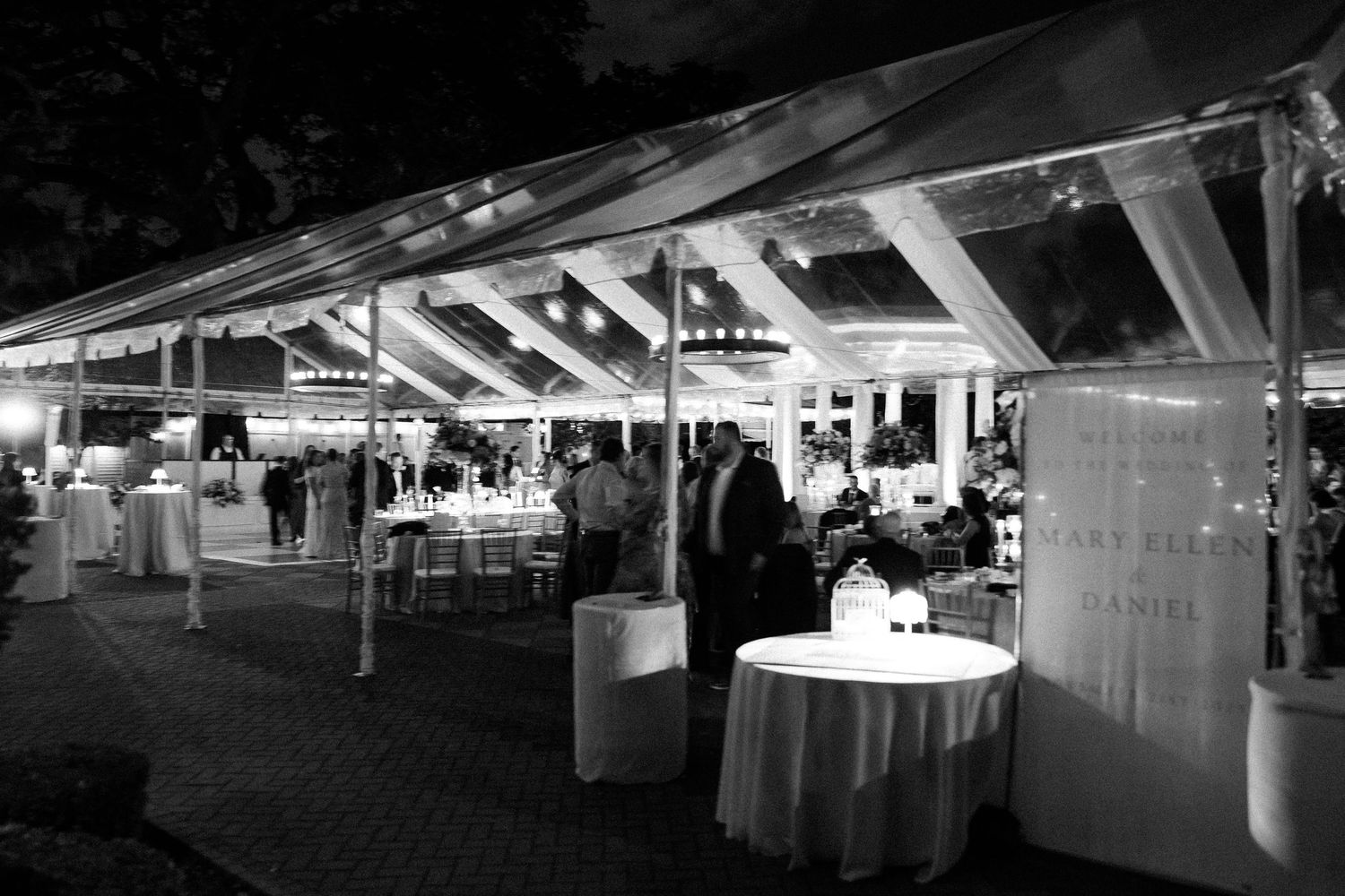 Black and white panoramic view of an elegant tented wedding reception space with tables and lighting.