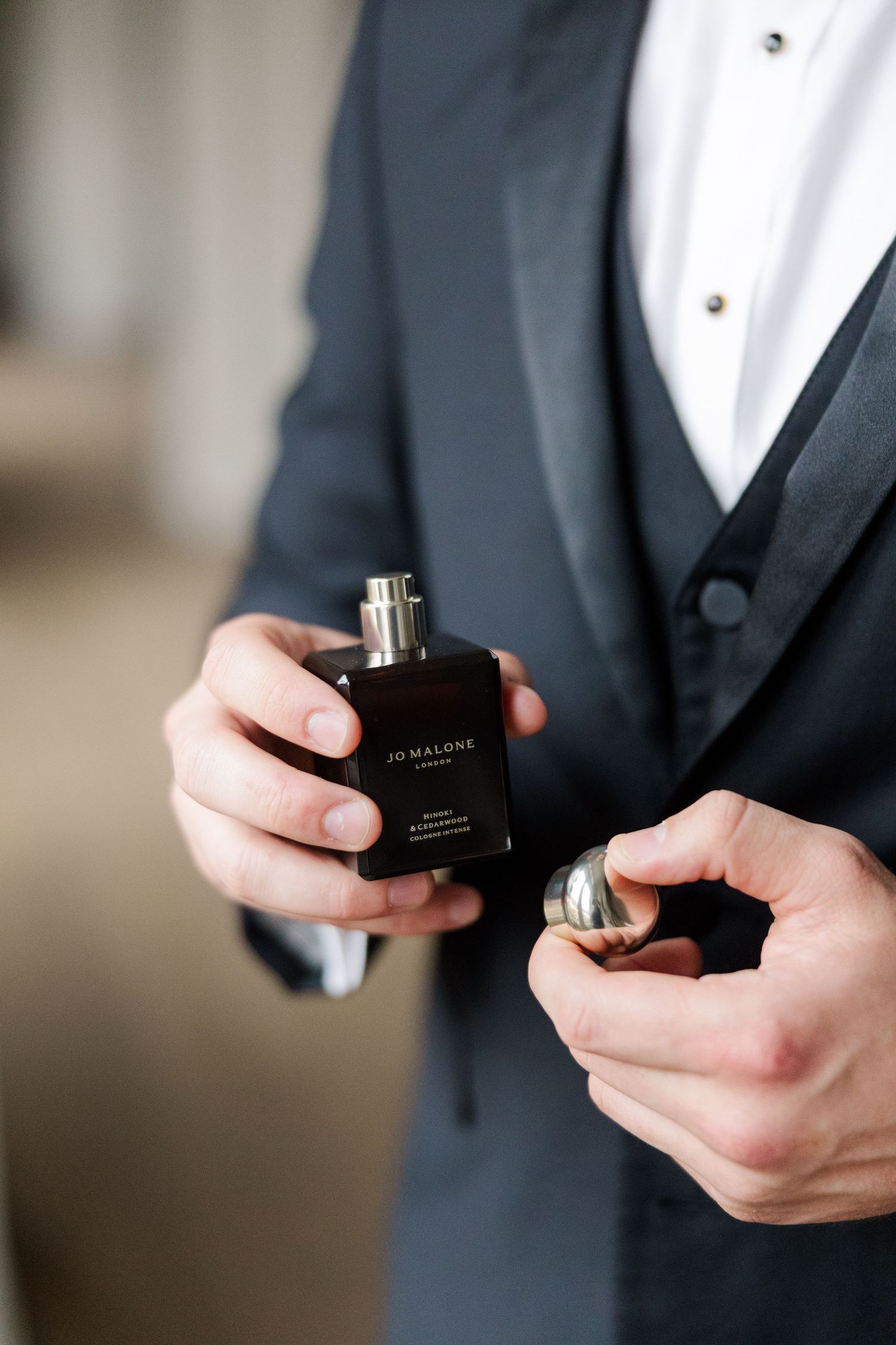 Close-up shot of hands holding a black perfume bottle against a formal tuxedo.
