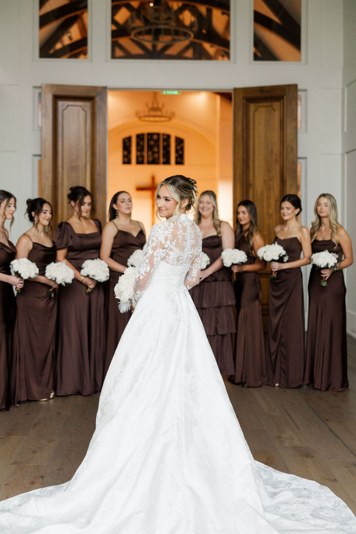Wedding party poses in elegant brown dresses while the bride stands out in a flowing white gown with dramatic train.
