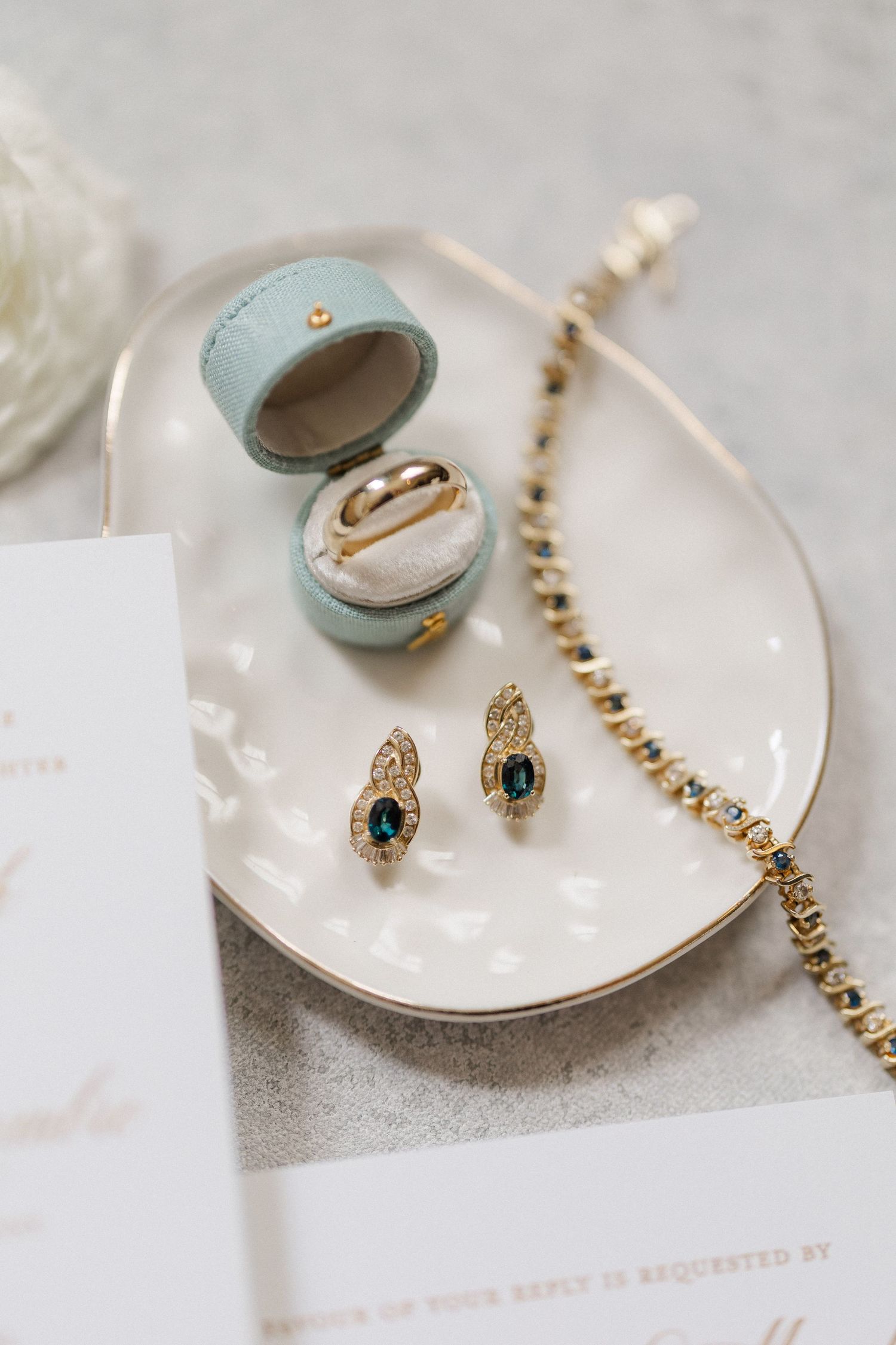 Elegant wedding jewelry flat lay featuring emerald earrings, gold bracelet, and wedding band in a mint velvet ring box.