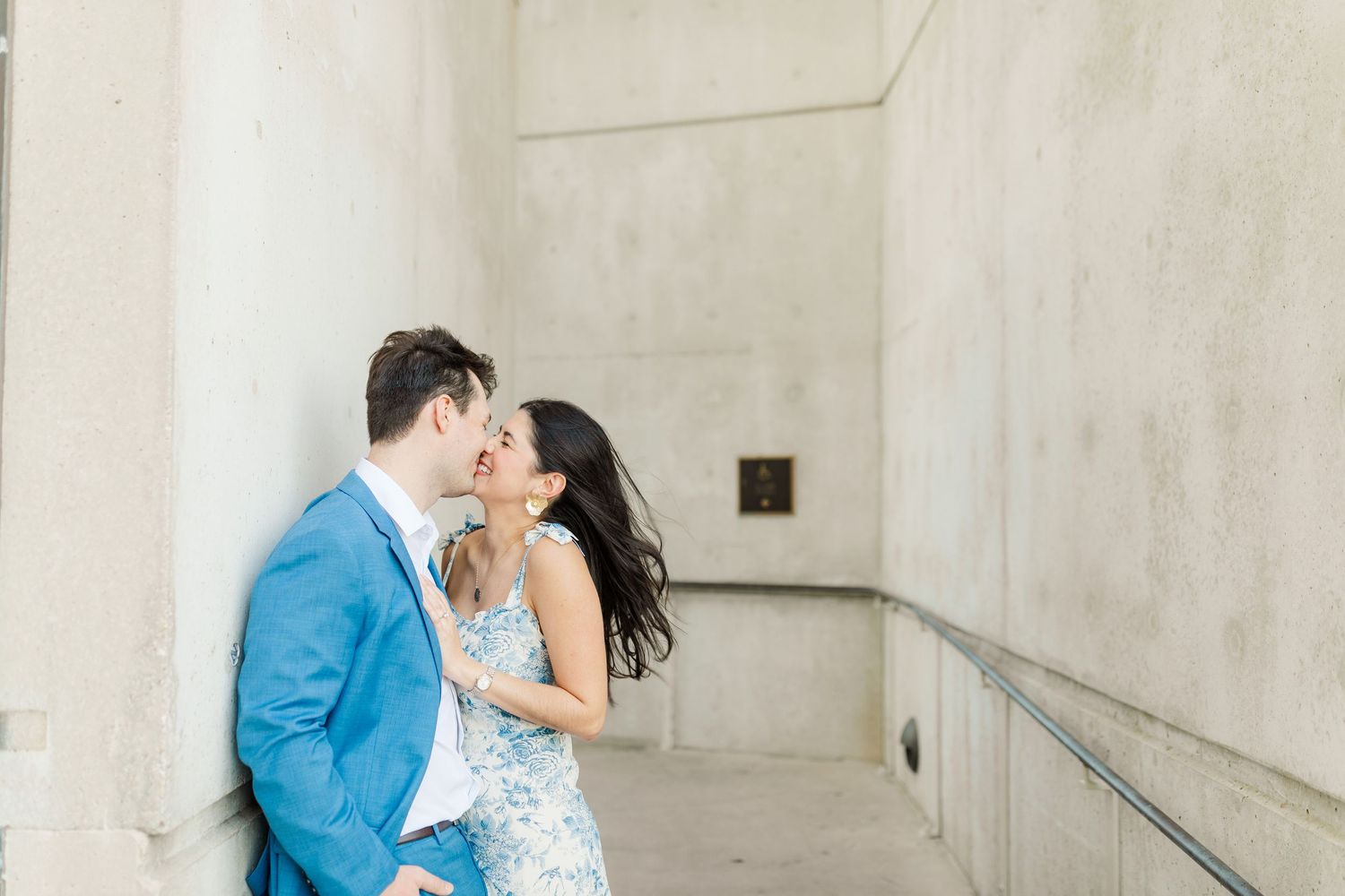 Romantic couple in blue and white outfits sharing a tender moment against a light colored wall.