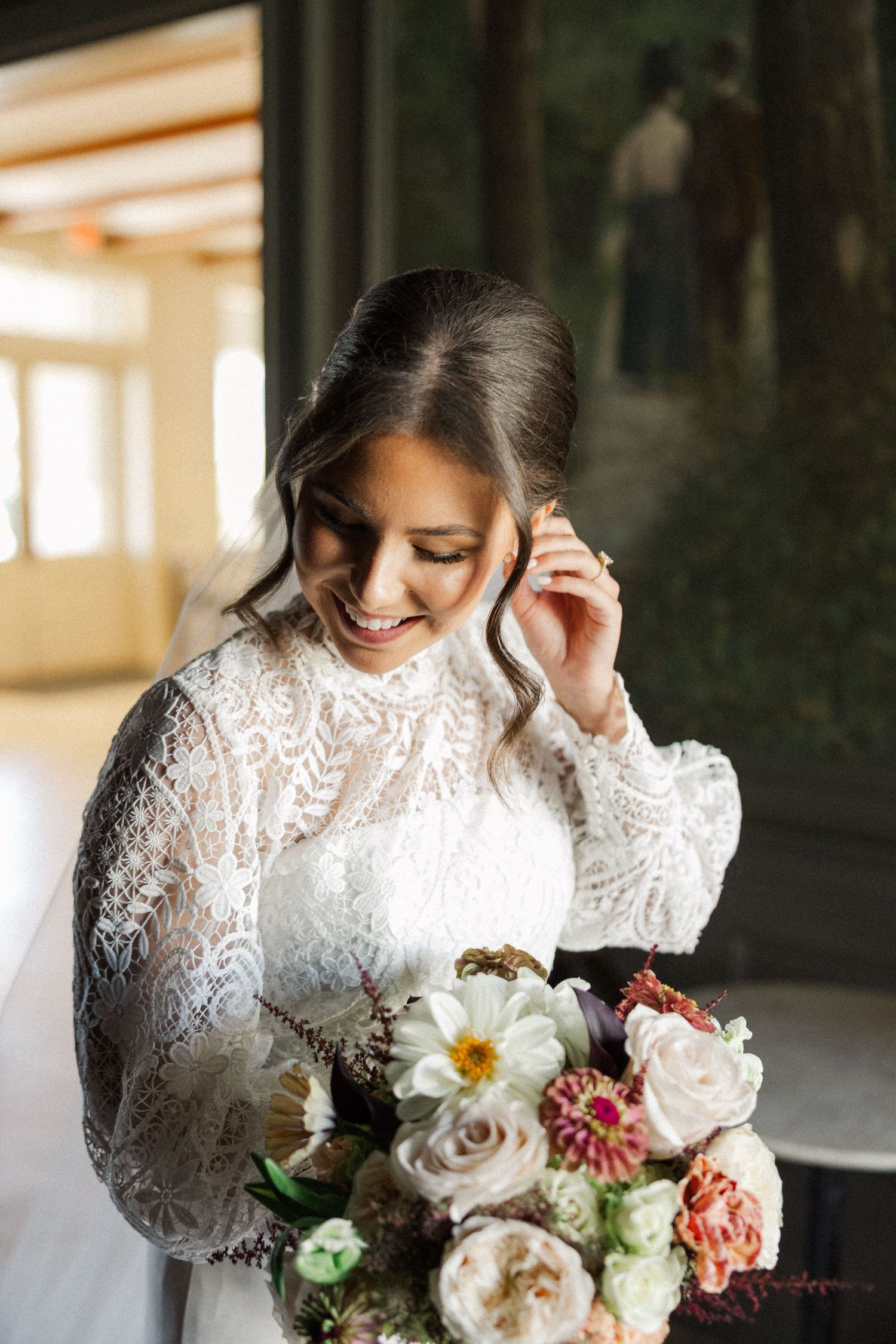 A bride in a long-sleeved lace wedding dress holds a romantic bouquet of pink, white and burgundy flowers.