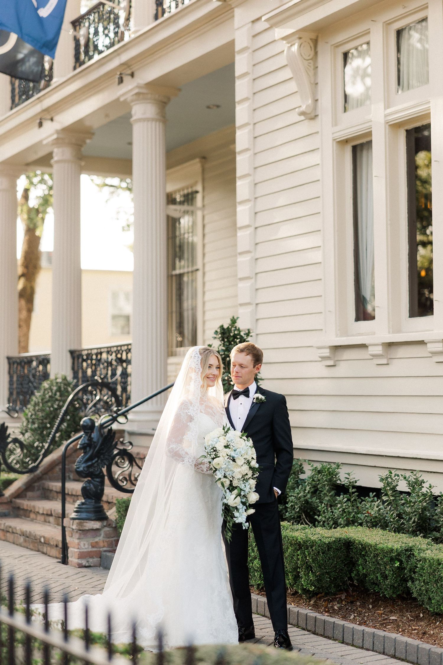 Elegant white columned mansion exterior serves as backdrop for formal wedding photos.