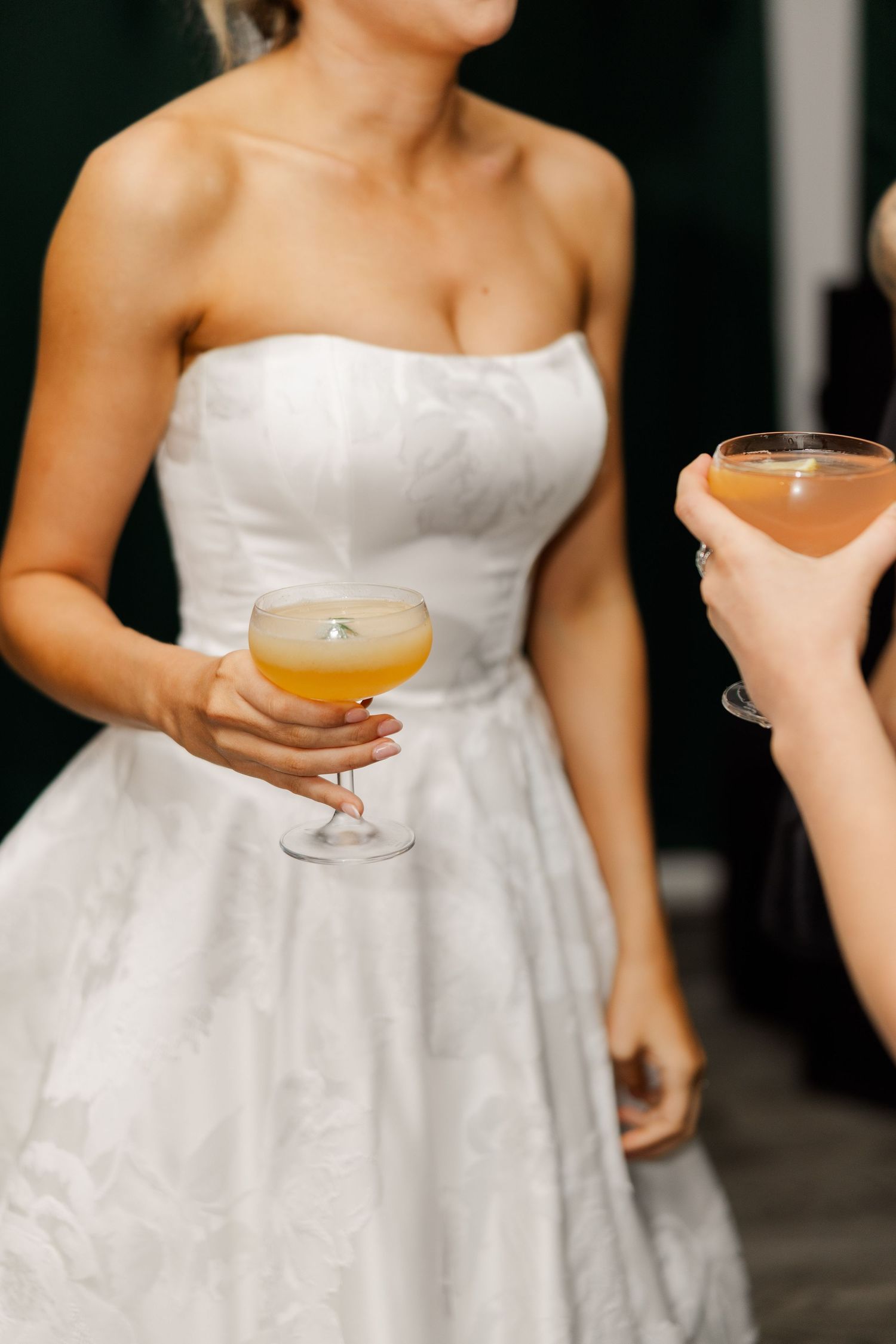 Close-up of a wedding dress and cocktail glass being held during reception celebrations.