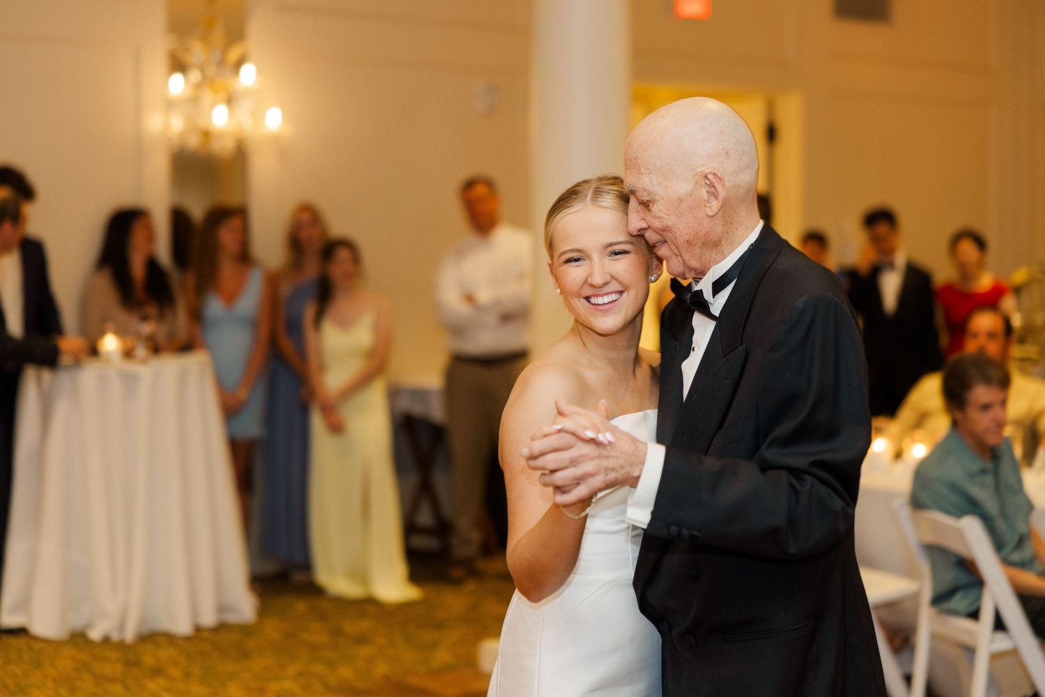 Wedding couple shares first dance in elegant ballroom surrounded by guests at their reception.