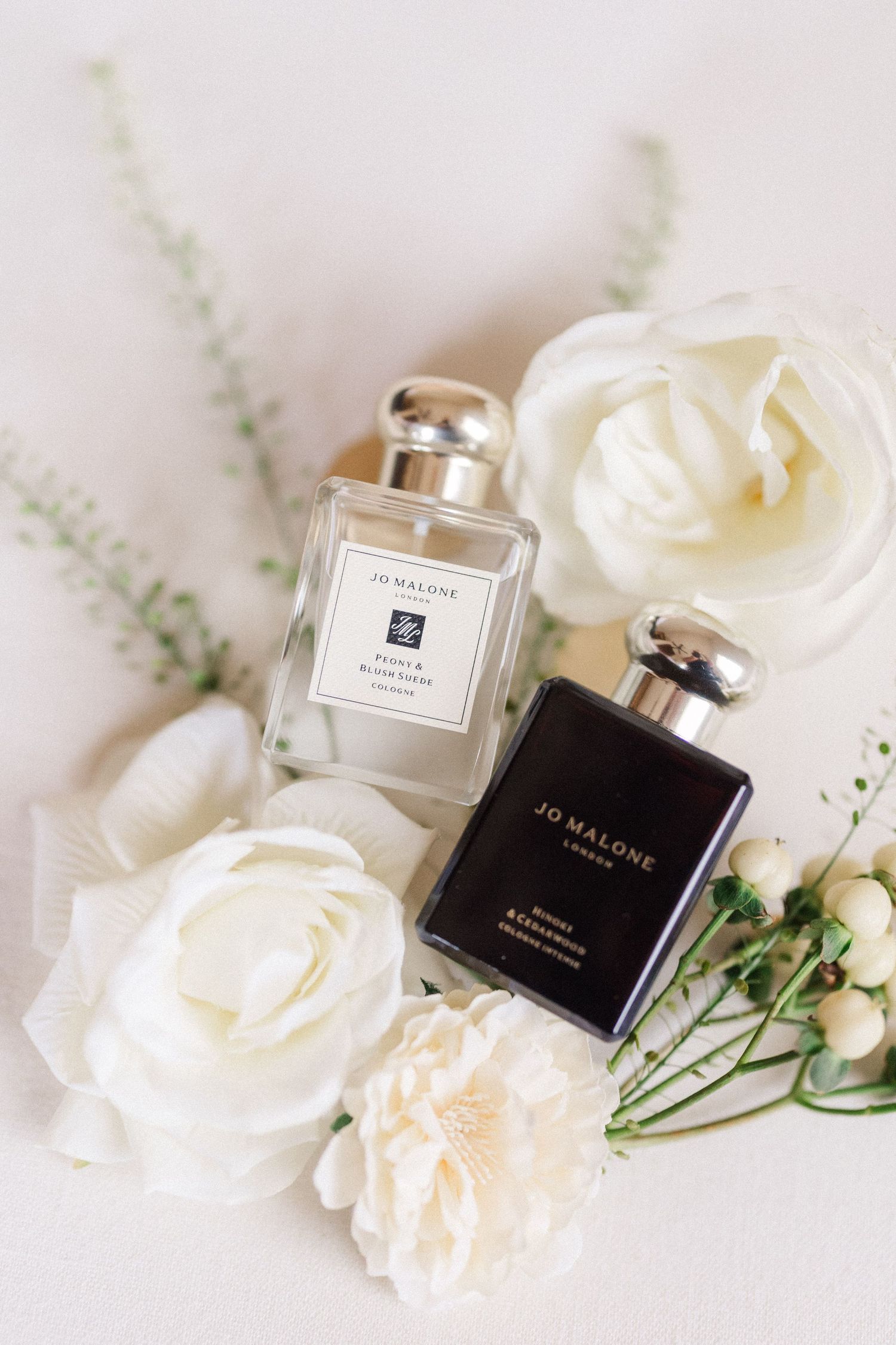 Elegant perfume bottles from Jo Malone and other luxury brands displayed with white roses and delicate greenery.