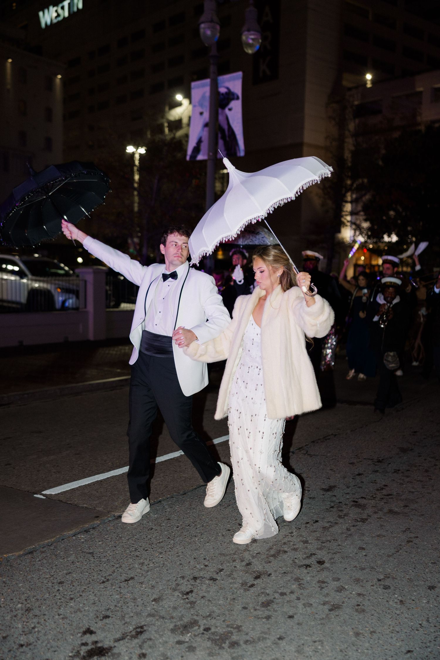 Couple walking with white parasols during nighttime wedding celebration.