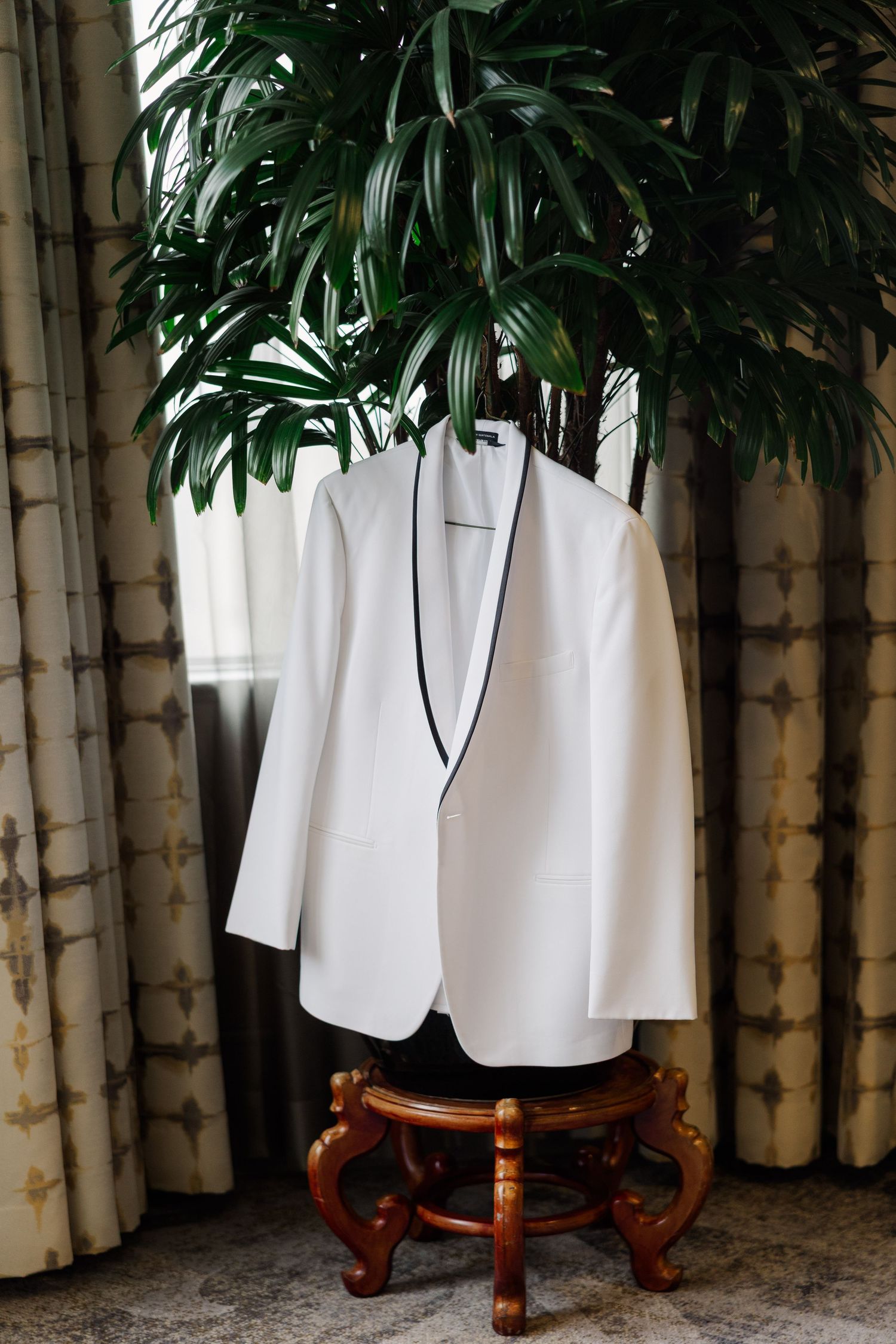 White suit jackets hanging among tropical palm leaves and bamboo decor.