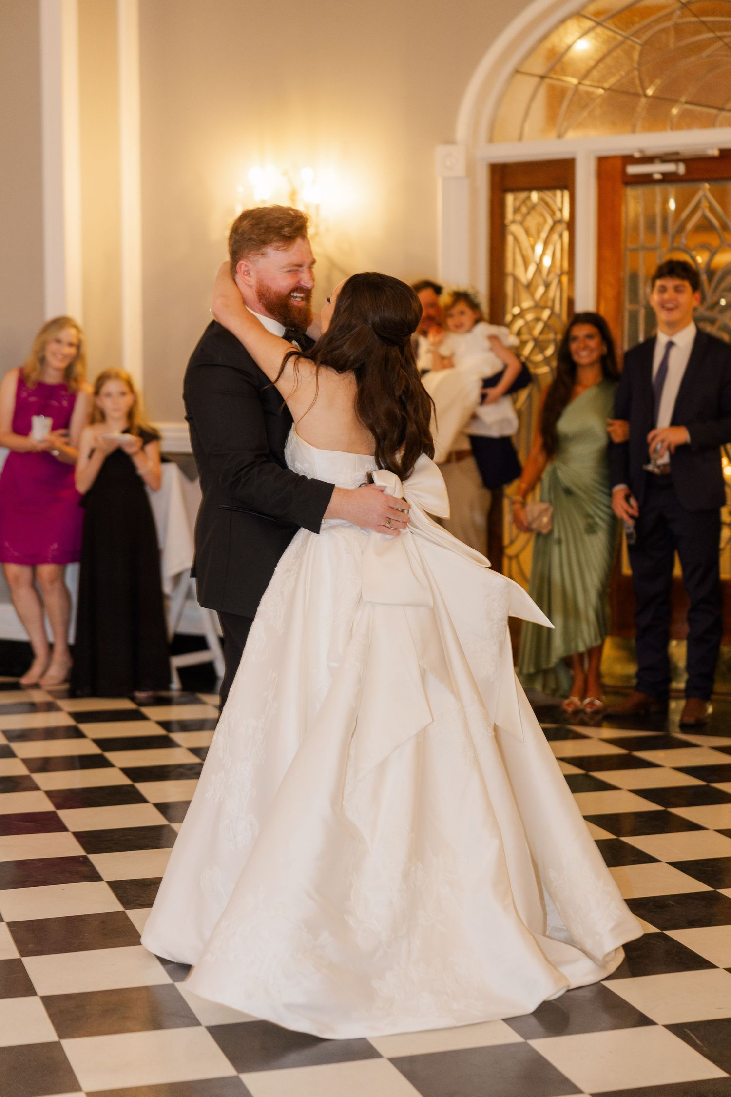 Couples dance on a classic black and white checkered ballroom floor at an elegant wedding reception.