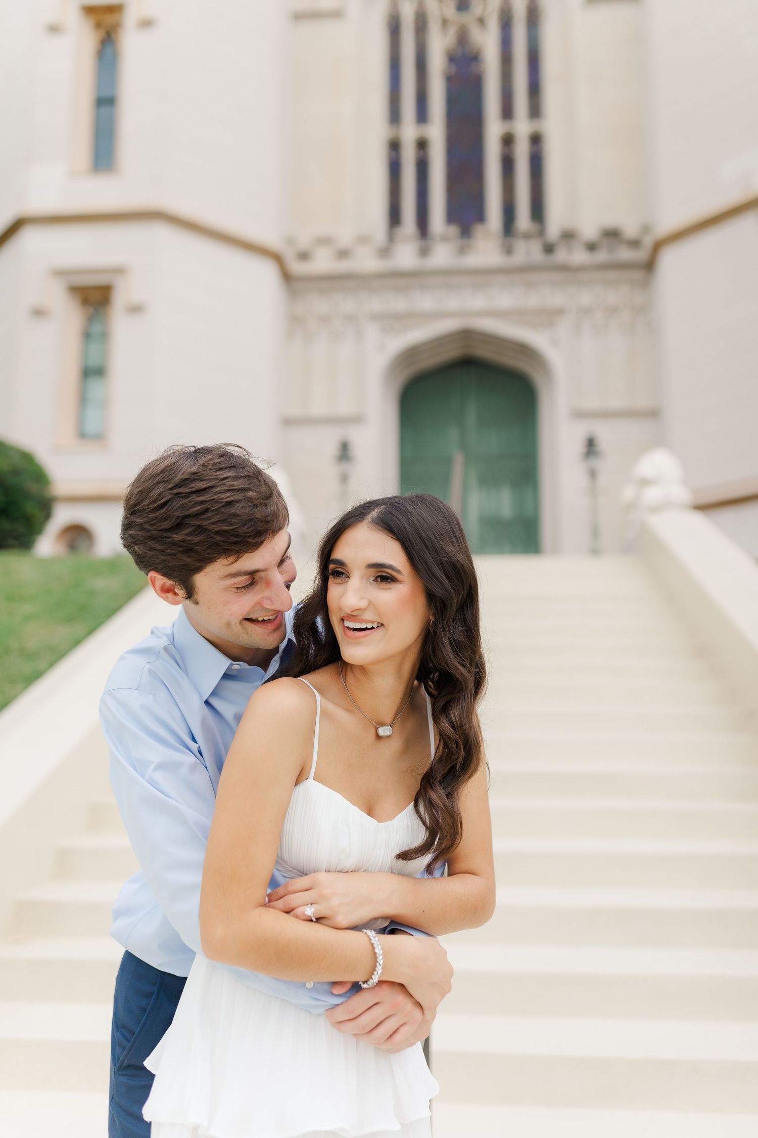 A romantic couple embraces on white church steps, with gothic architecture and a green door visible in the background.