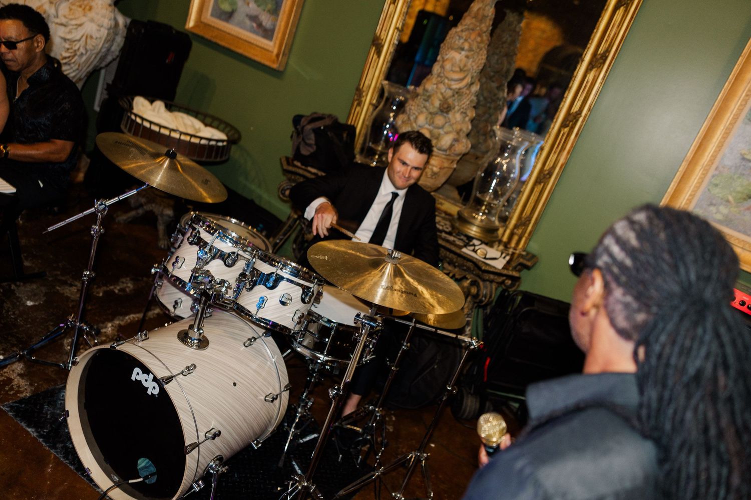Drummer performing at elegant wedding reception with gold mirror decor in background.