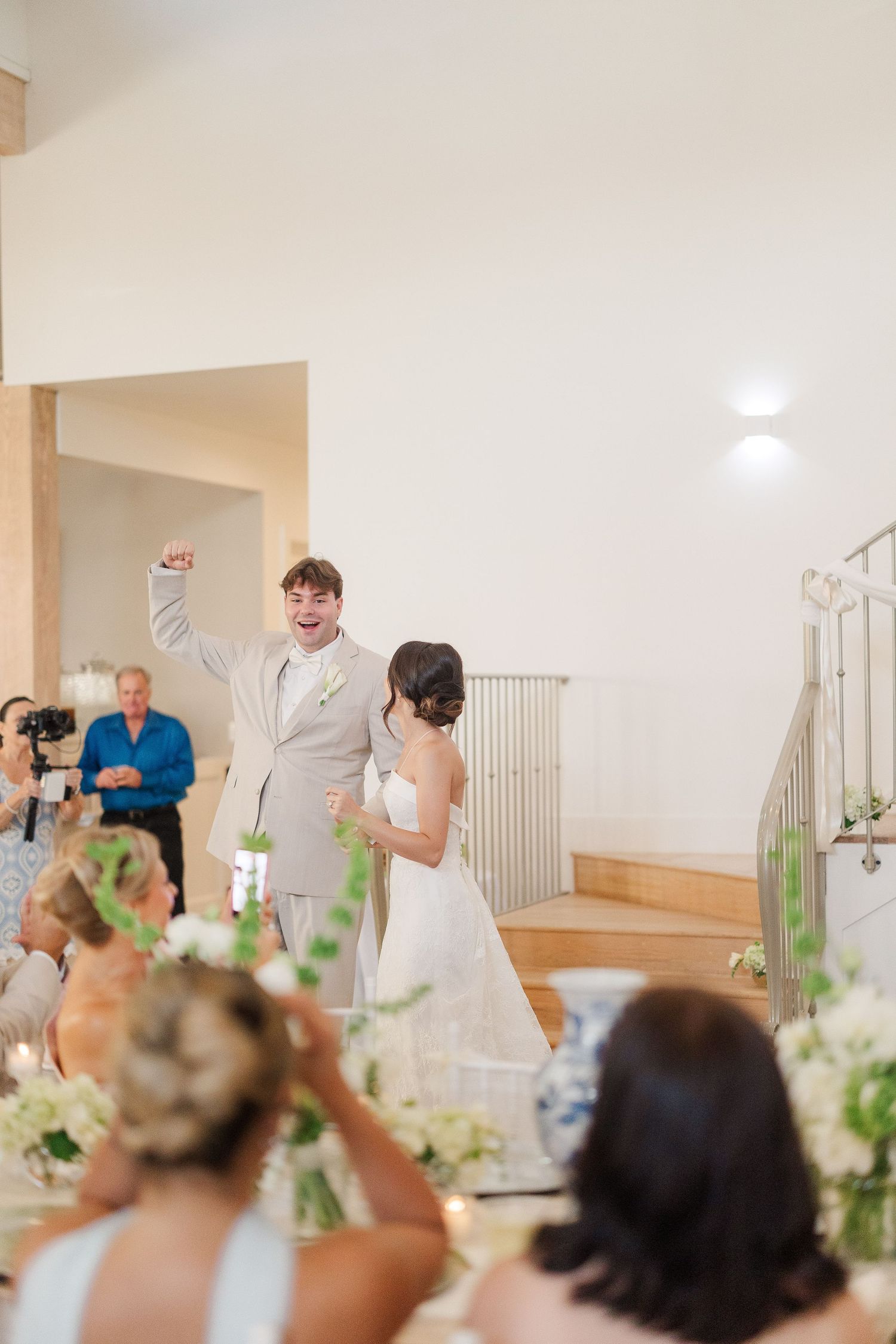 Excited groom raises fist as he and bride make grand reception entrance before seated wedding guests.