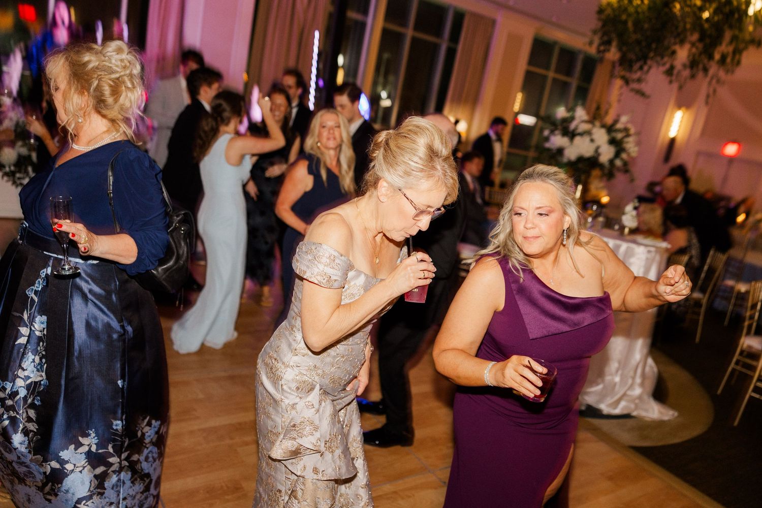 Guests in formal attire dancing and celebrating at elegant wedding reception with pink ambient lighting.