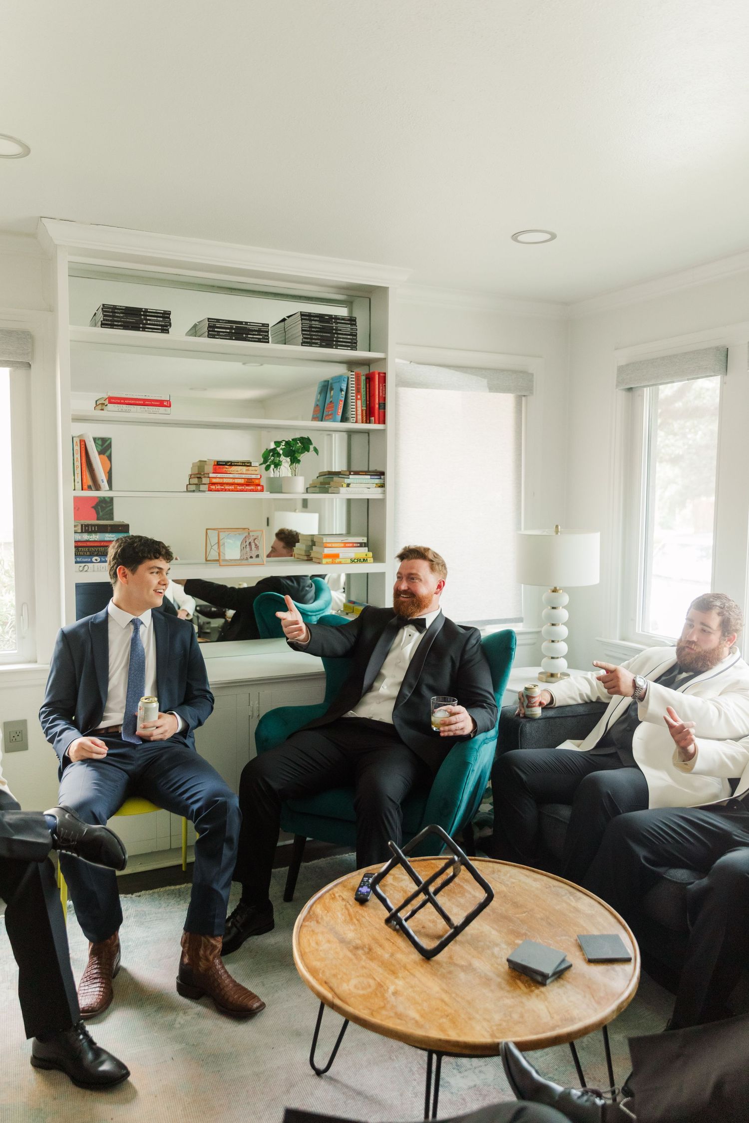 Wedding party relaxing in a modern living room with turquoise chairs and a round wooden table.