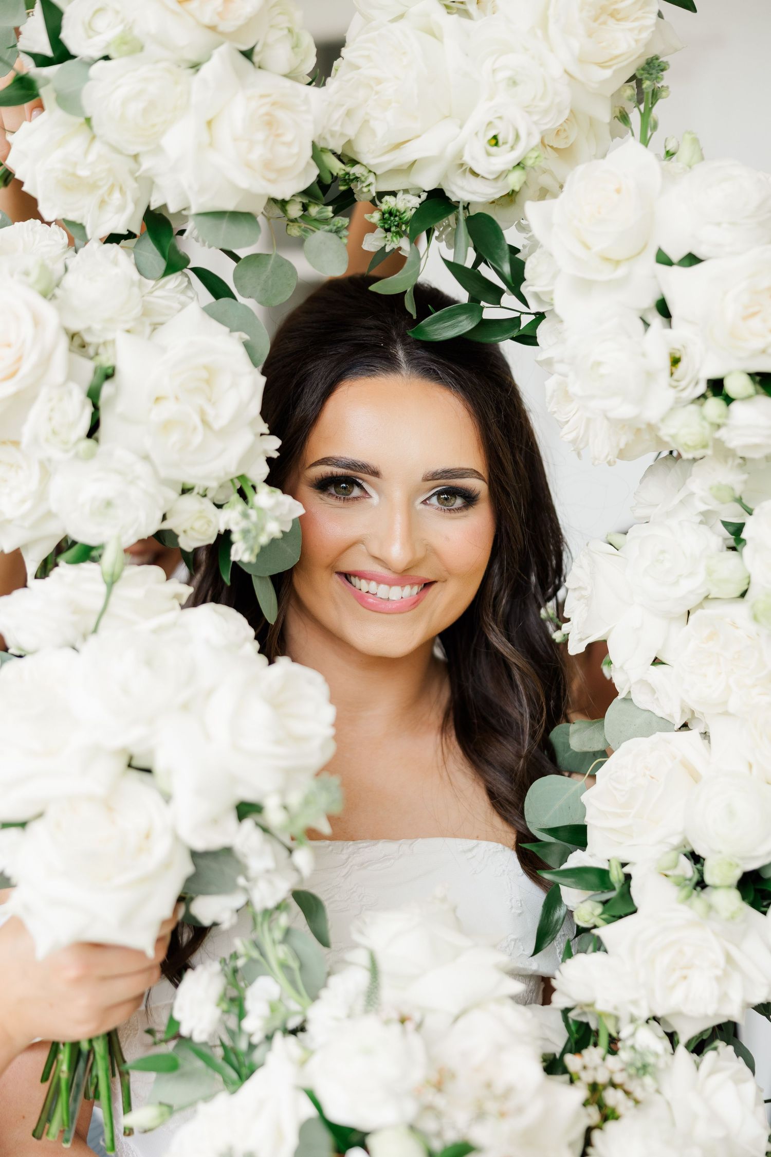 Bridal portrait with white roses and greenery creating an elegant floral backdrop.