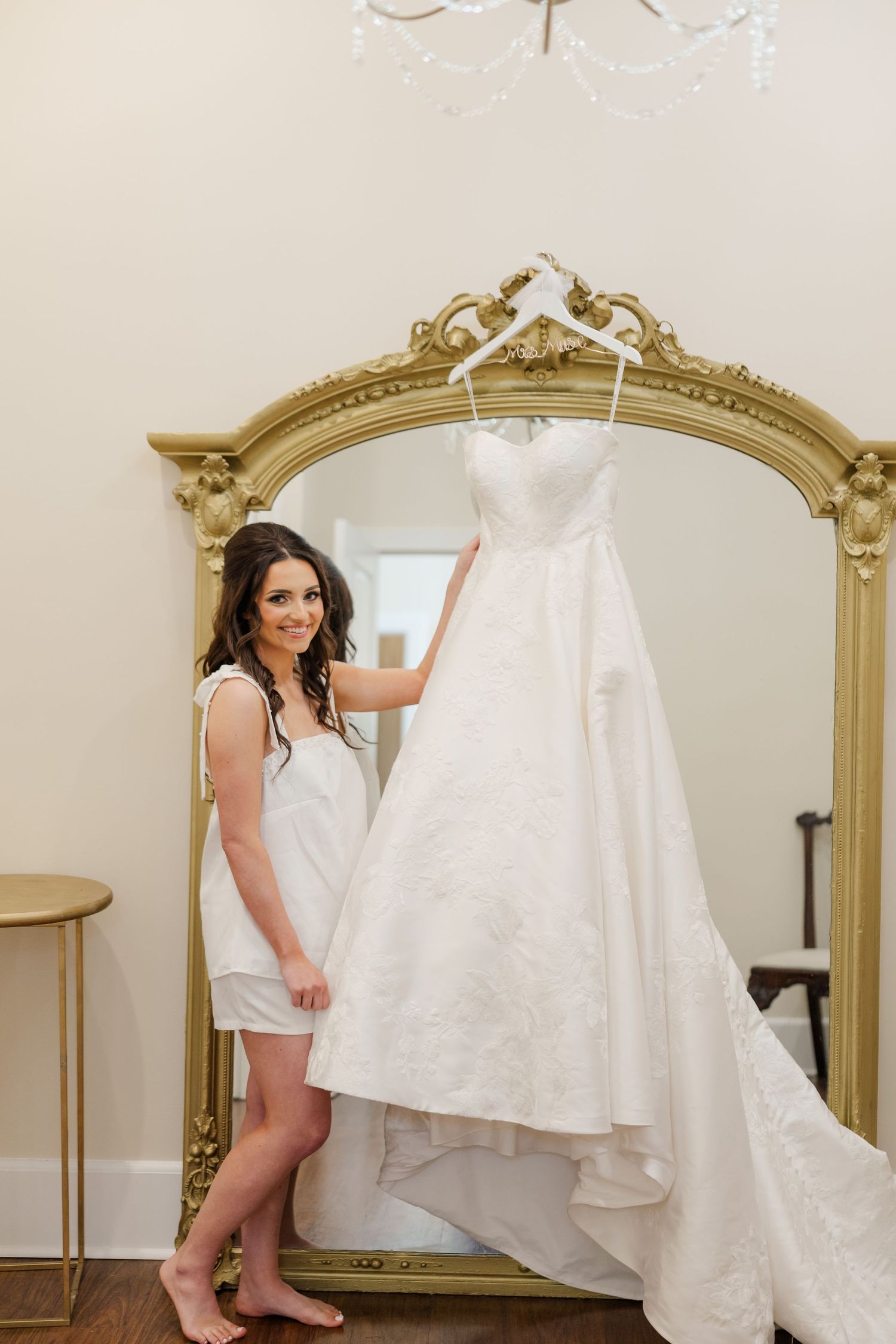 Wedding dress preparation scene with an ornate gold mirror and white gown.