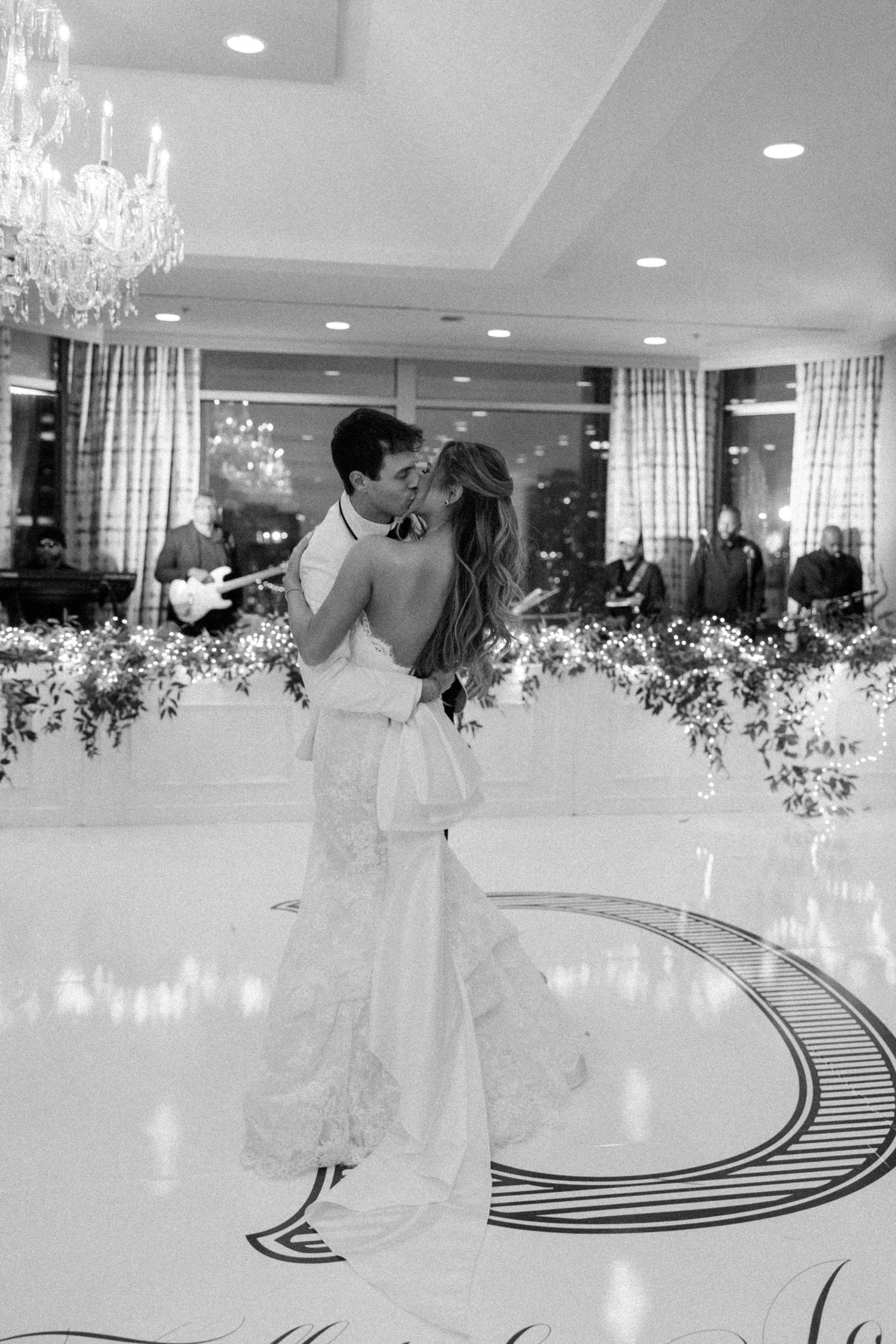A black and white photo of a couple sharing their first dance in an elegant ballroom.