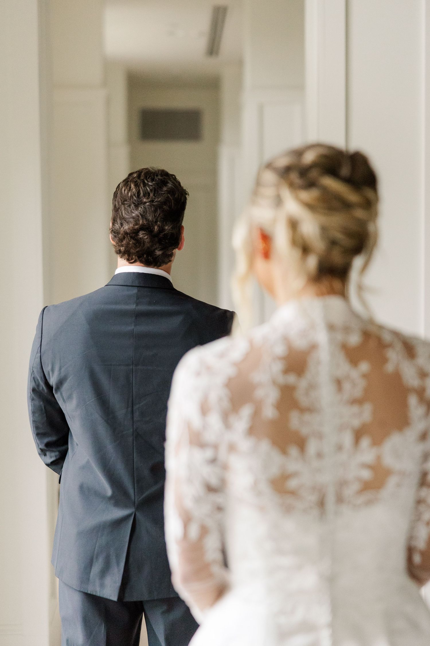 A couple shares their first look moment in a bright hallway with white walls.